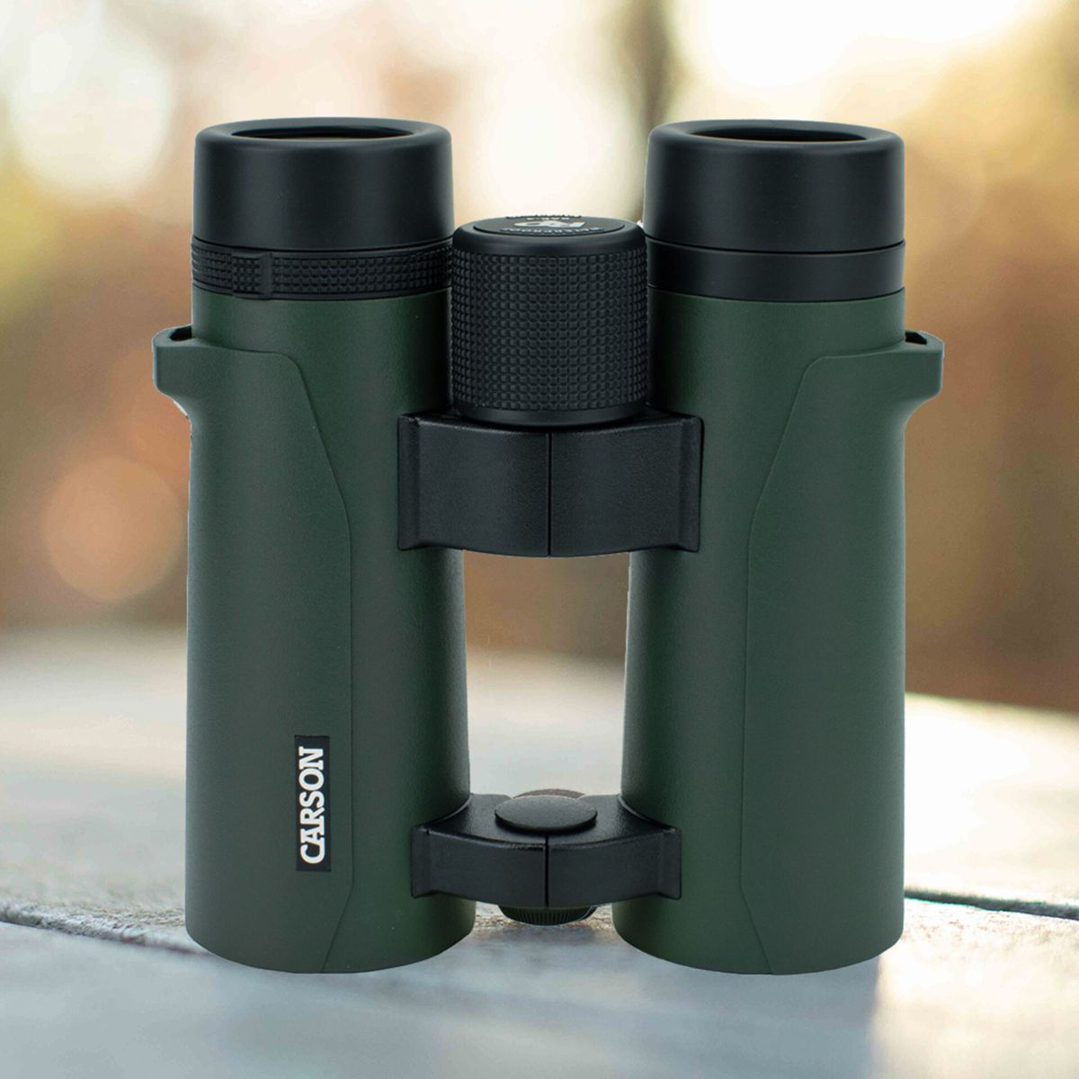 Binocolo verde Carson con rotella di messa a fuoco e tappi neri su tavolo.