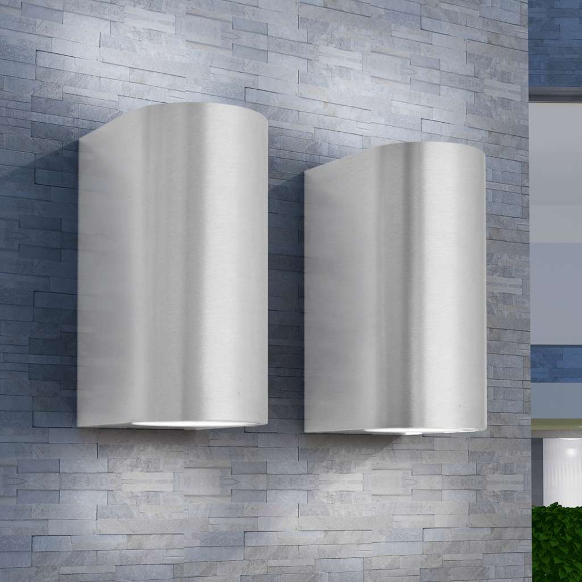 Zwei moderne silberne Wandleuchten beleuchten eine graue Steinwand.