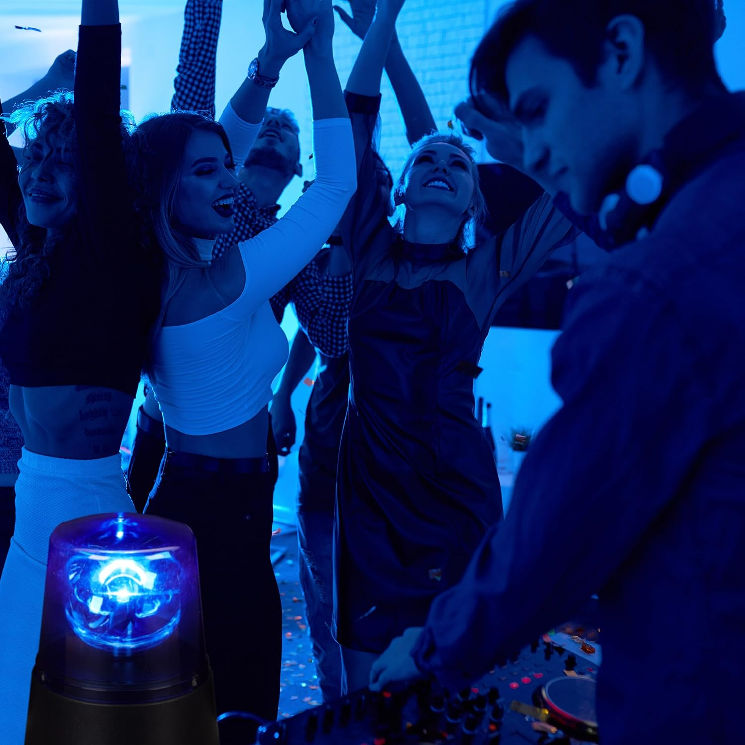Menschen tanzen in einem Club mit blauer Beleuchtung und einem DJ-Pult im Vordergrund.