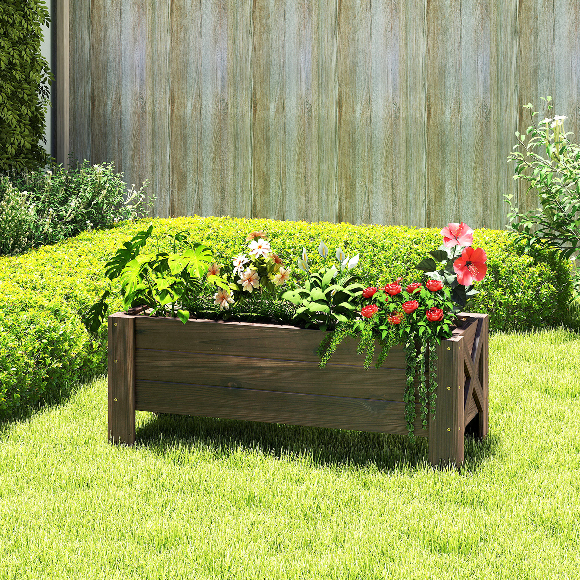 Una jardinera marrón con flores coloridas y plantas verdes sobre un césped soleado.