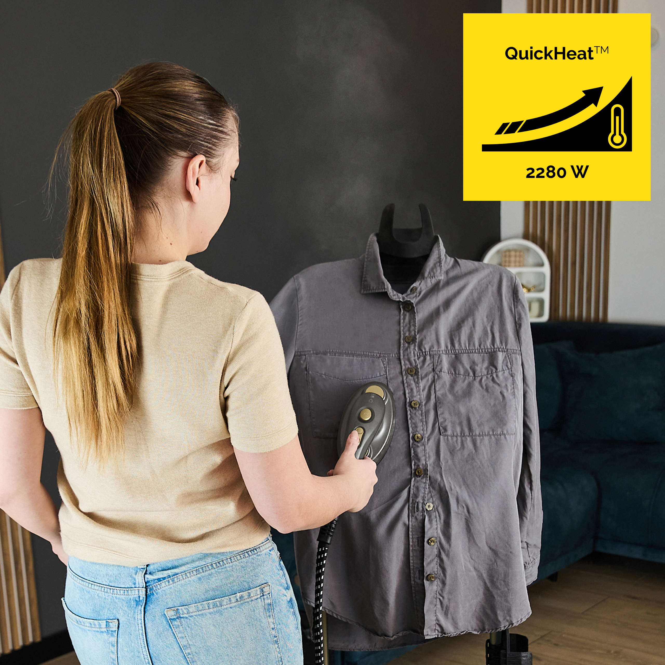 Kobieta prasuje szarą koszulę ręczną parownicą. Para unosi się.