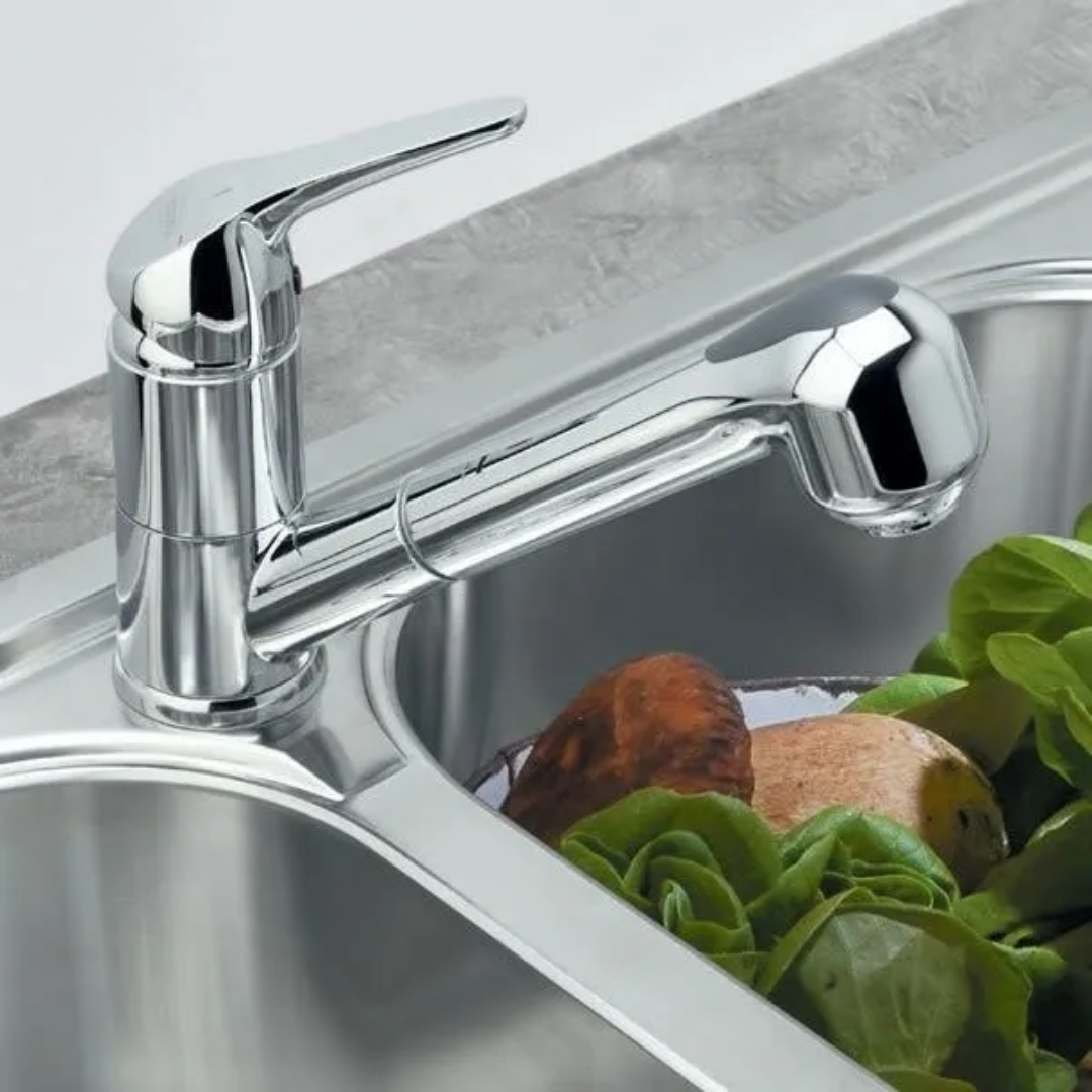 Un rubinetto cromato con beccuccio estraibile sopra un lavello con lattuga e verdure a radice.