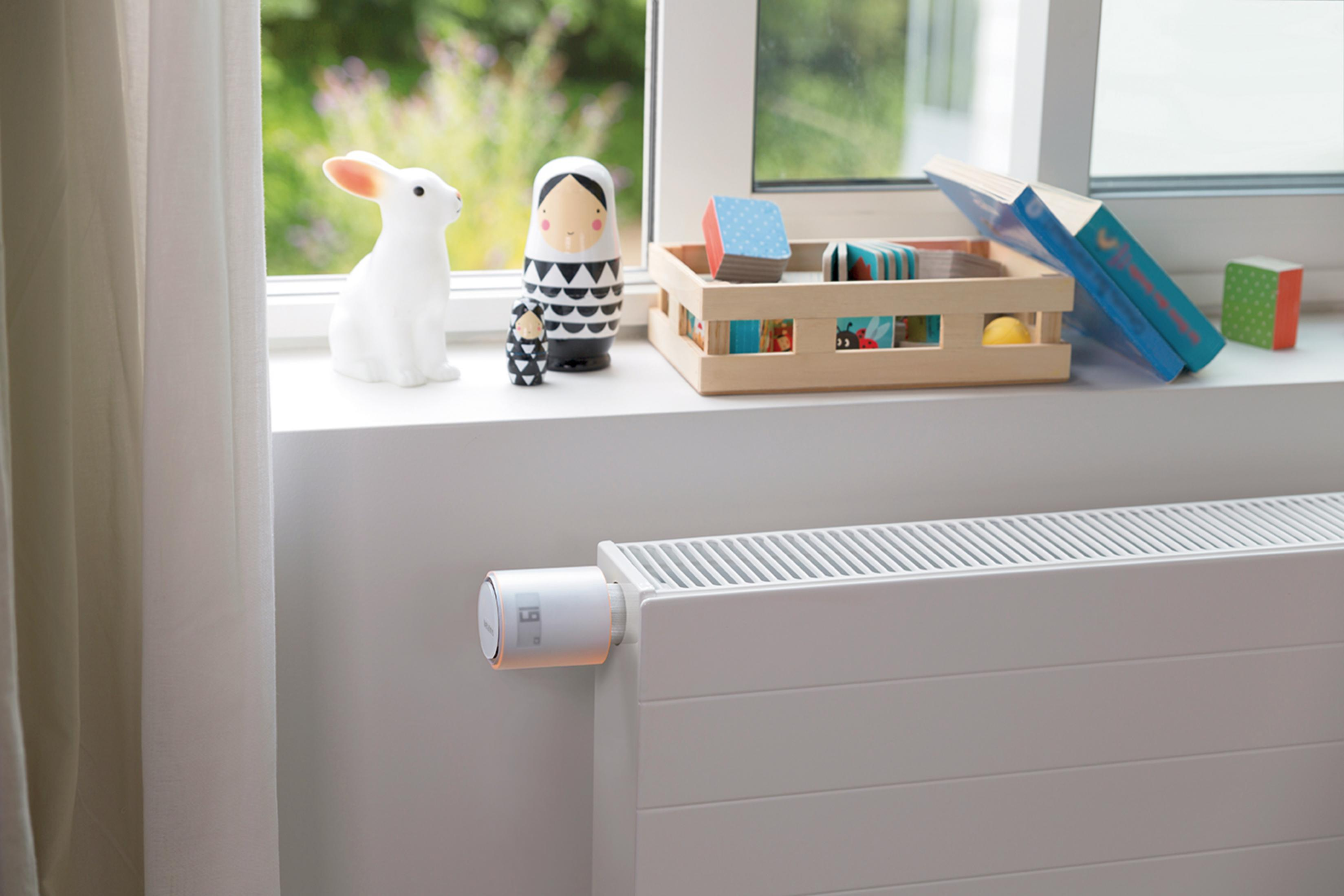 A white radiator thermostat next to toys on a windowsill.