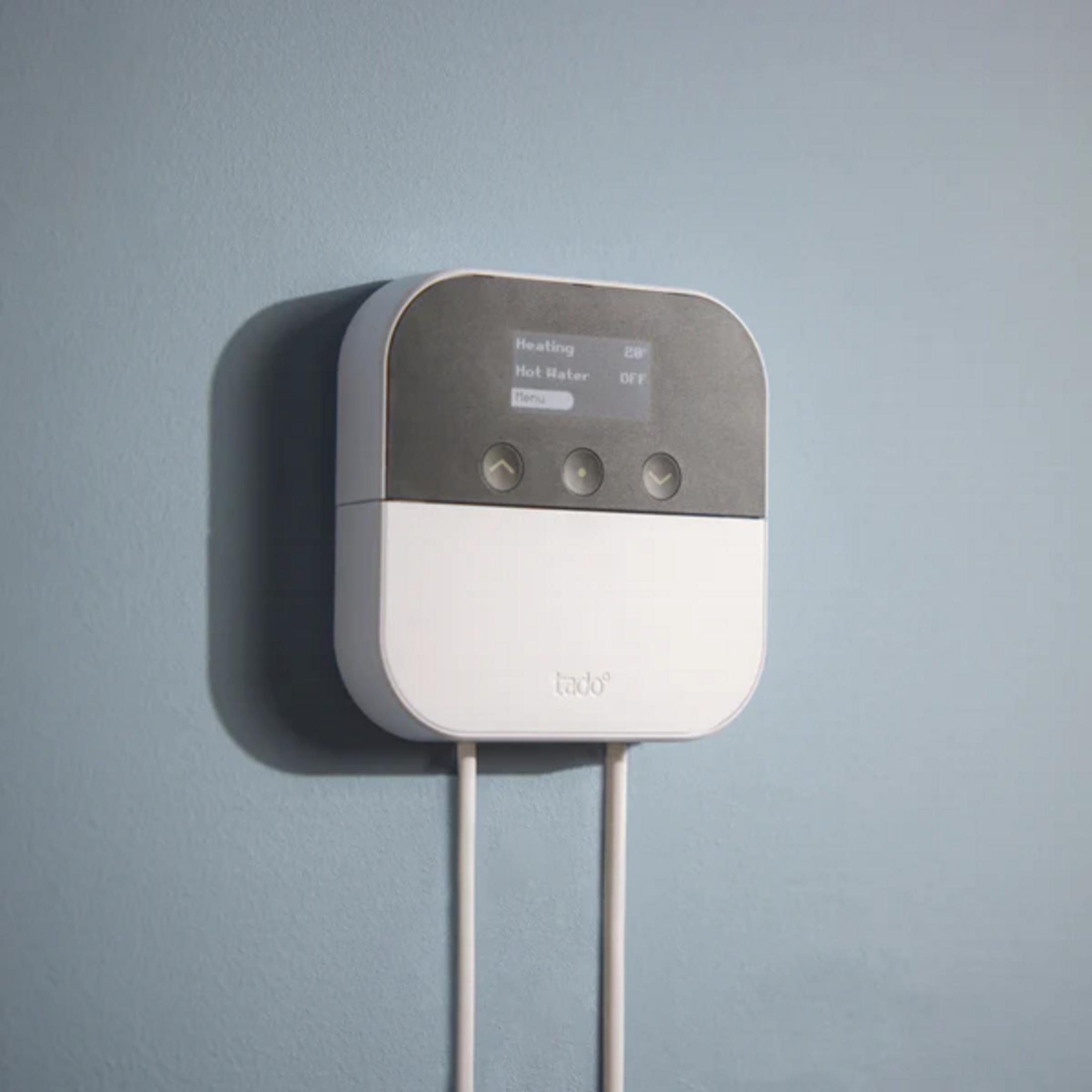 A white and gray Tado device with screen and buttons on a blue wall.