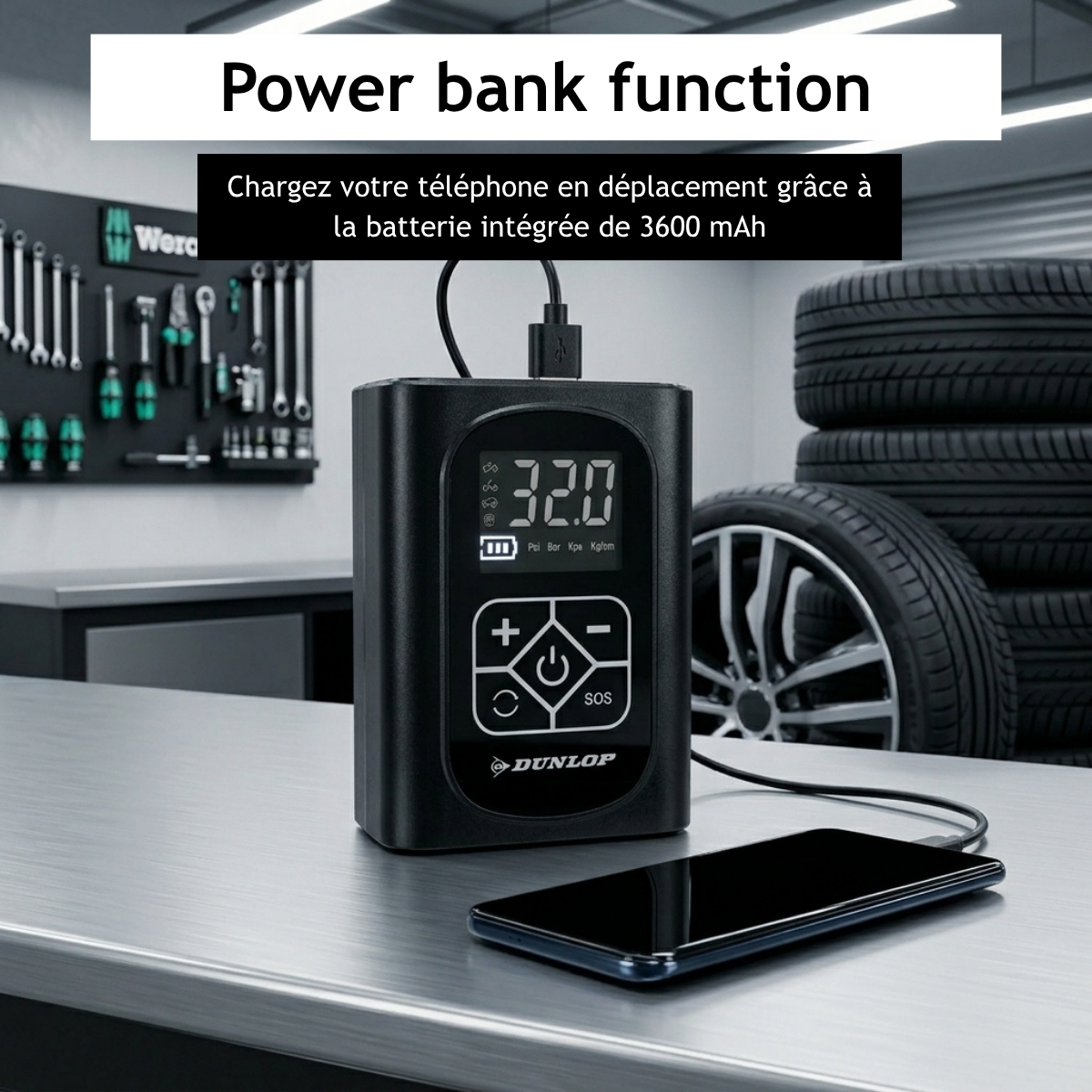 Zwarte powerbank met display en telefoon op tafel, banden op achtergrond.