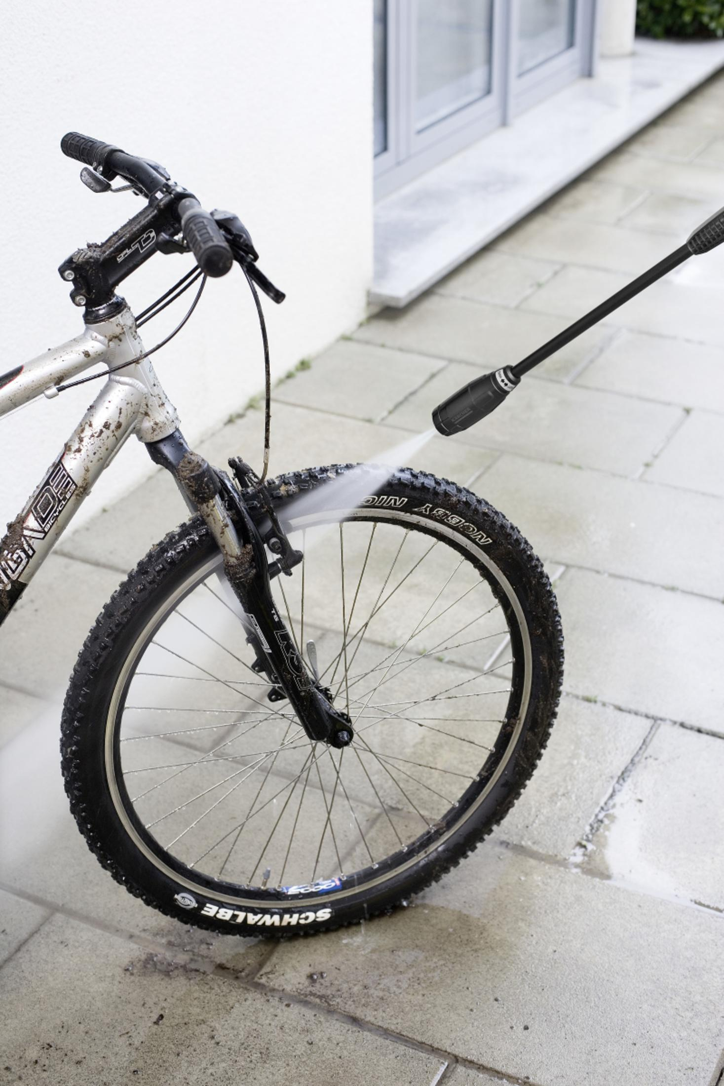 Een vieze fiets wordt schoongespoten met een hogedrukreiniger.