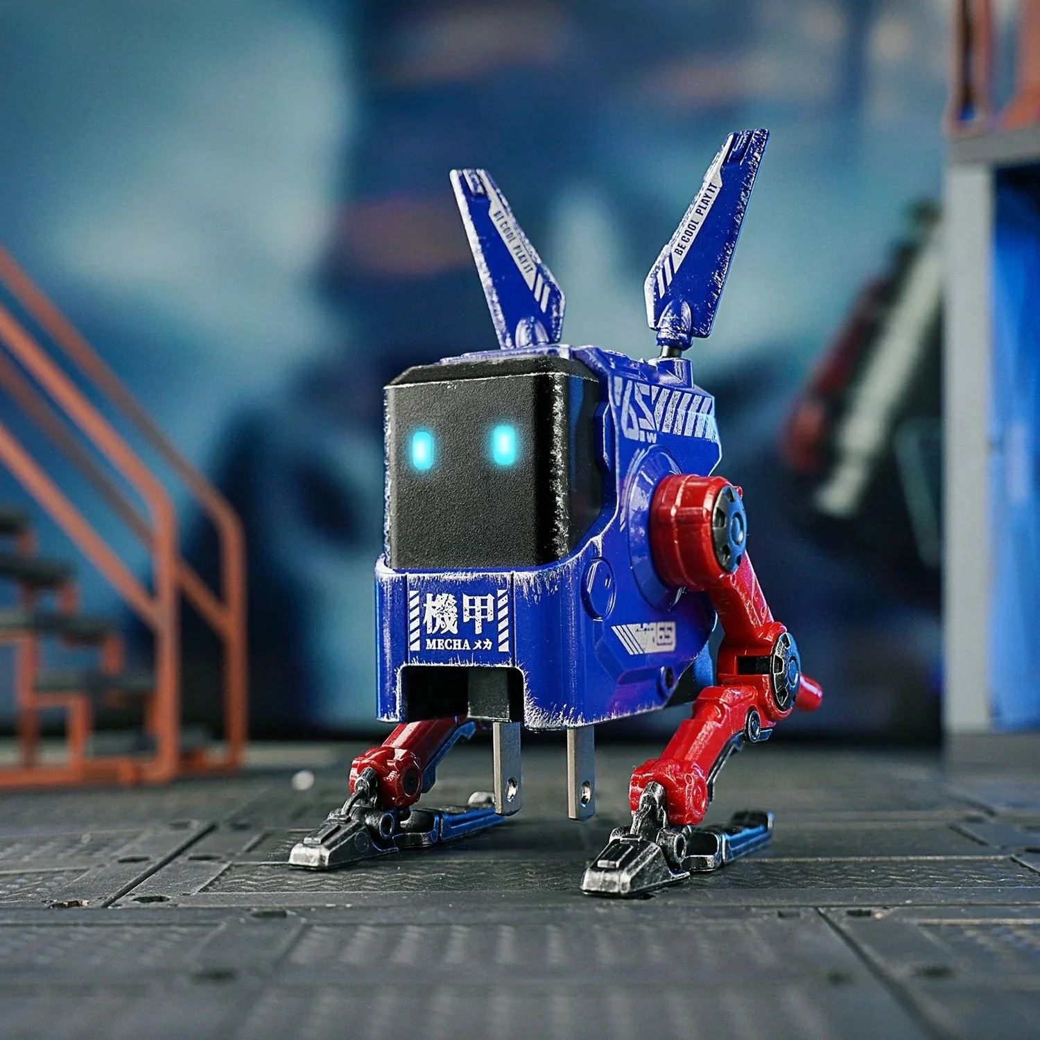 Niebieski robot z czerwonymi kończynami i świecącymi oczami stoi na ciemnej podłodze.