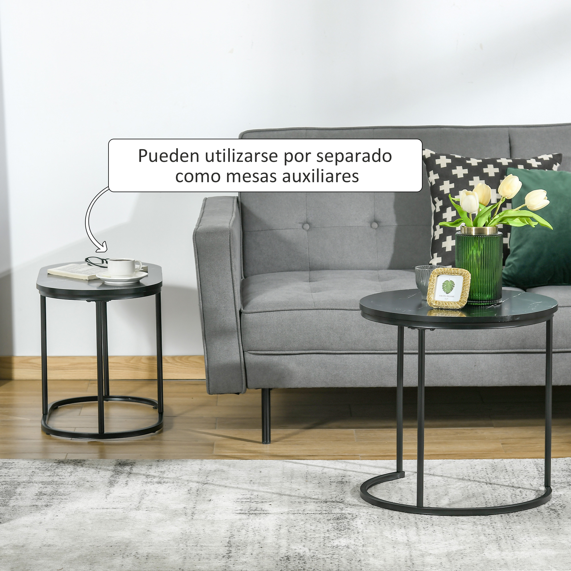 Dos mesas auxiliares redondas frente a un sofá gris con cojines y flores.