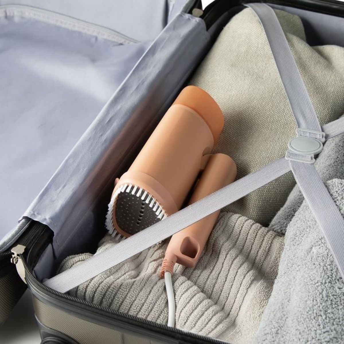 Un vaporizzatore portatile color pesca giace in una valigia accanto ai vestiti.