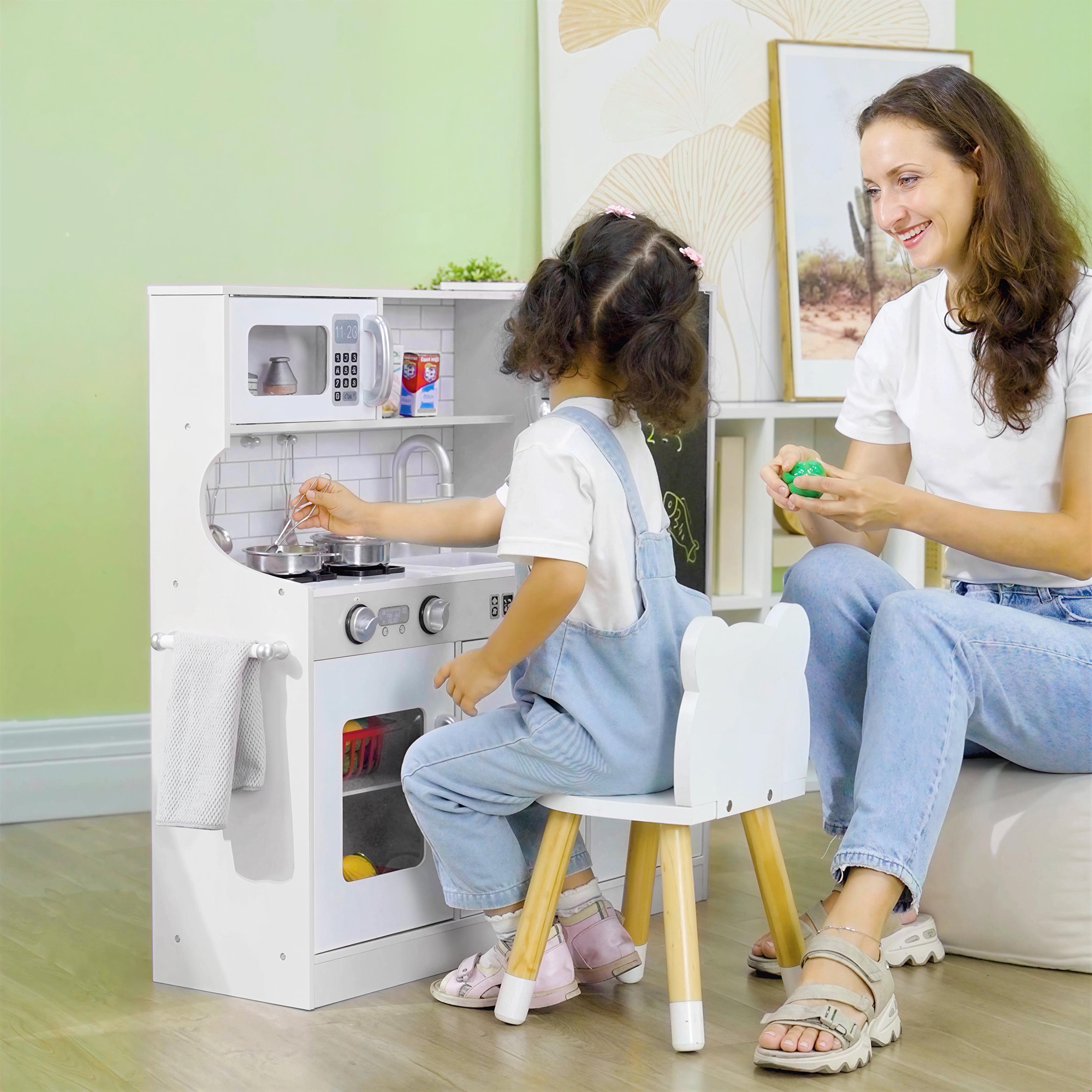 Mujer y niña juegan con cocina de juguete. Niña cocina, mujer sostiene bola verde.
