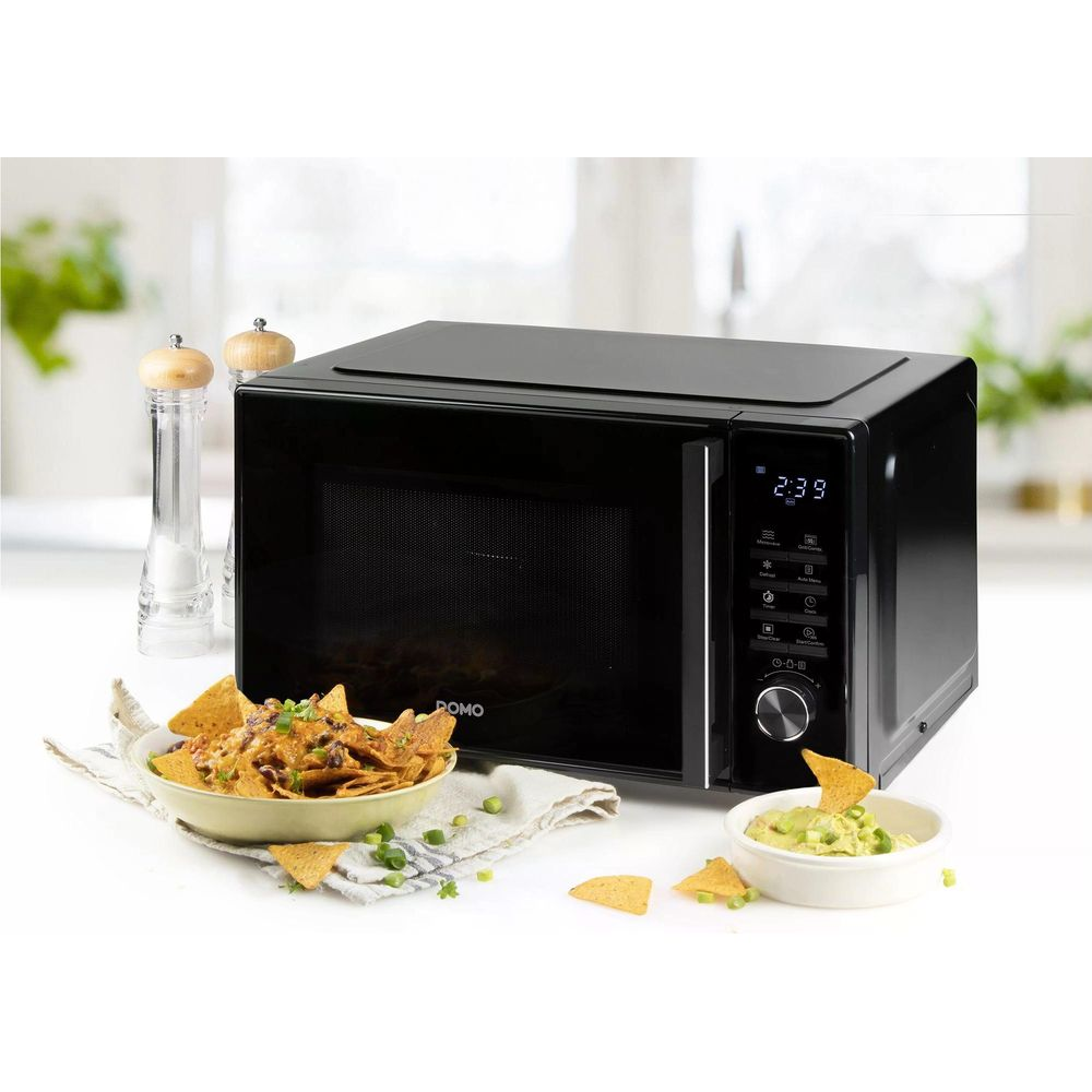 Micro-ondes noir avec un bol de nachos et du guacamole à côté.