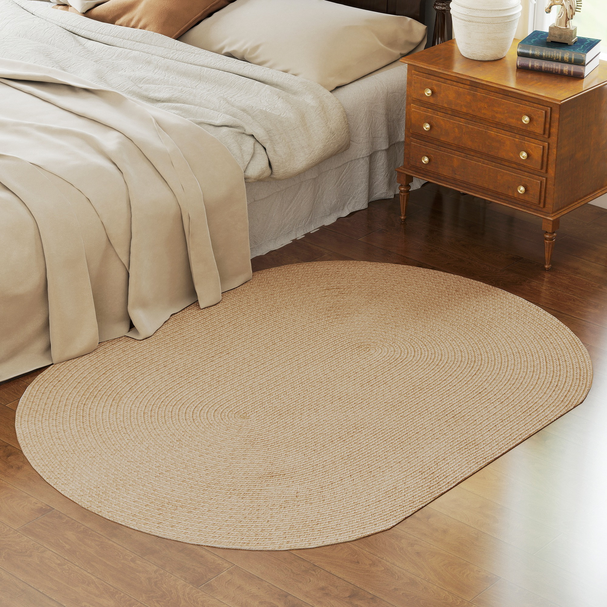 Una alfombra ovalada beige sobre suelo de madera junto a una cama.