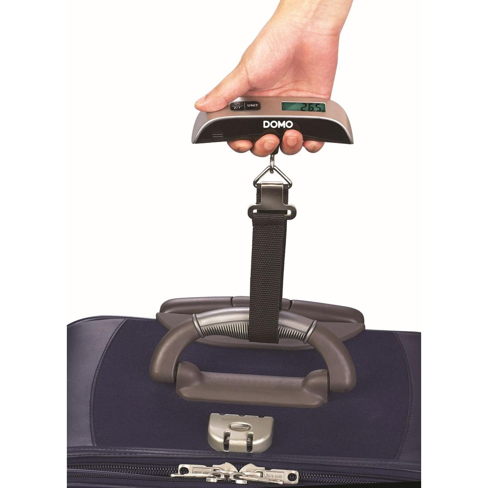 Eine Hand hält eine digitale Gepäckwaage über einem Koffer.