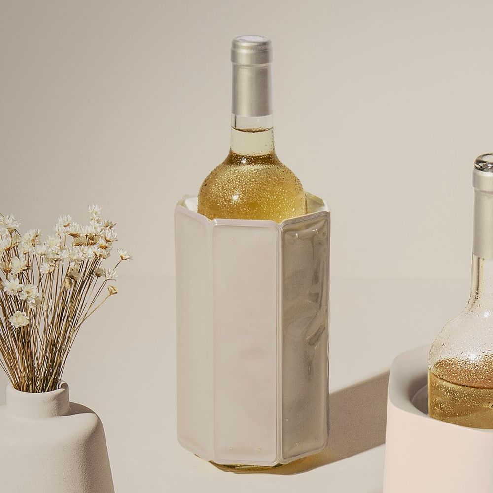 Una bottiglia di vino bianco in un secchiello per il ghiaccio accanto a un vaso di fiori secchi.