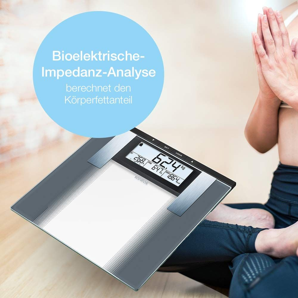 Waga łazienkowa z wyświetlaczem pokazuje 62,4 kg. Obok siedzi osoba w pozycji siedzącej.