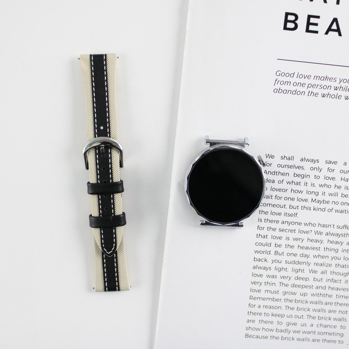 Un cinturino per orologio color crema con strisce nere e una cassa smartwatch argentata giacciono su un libro.