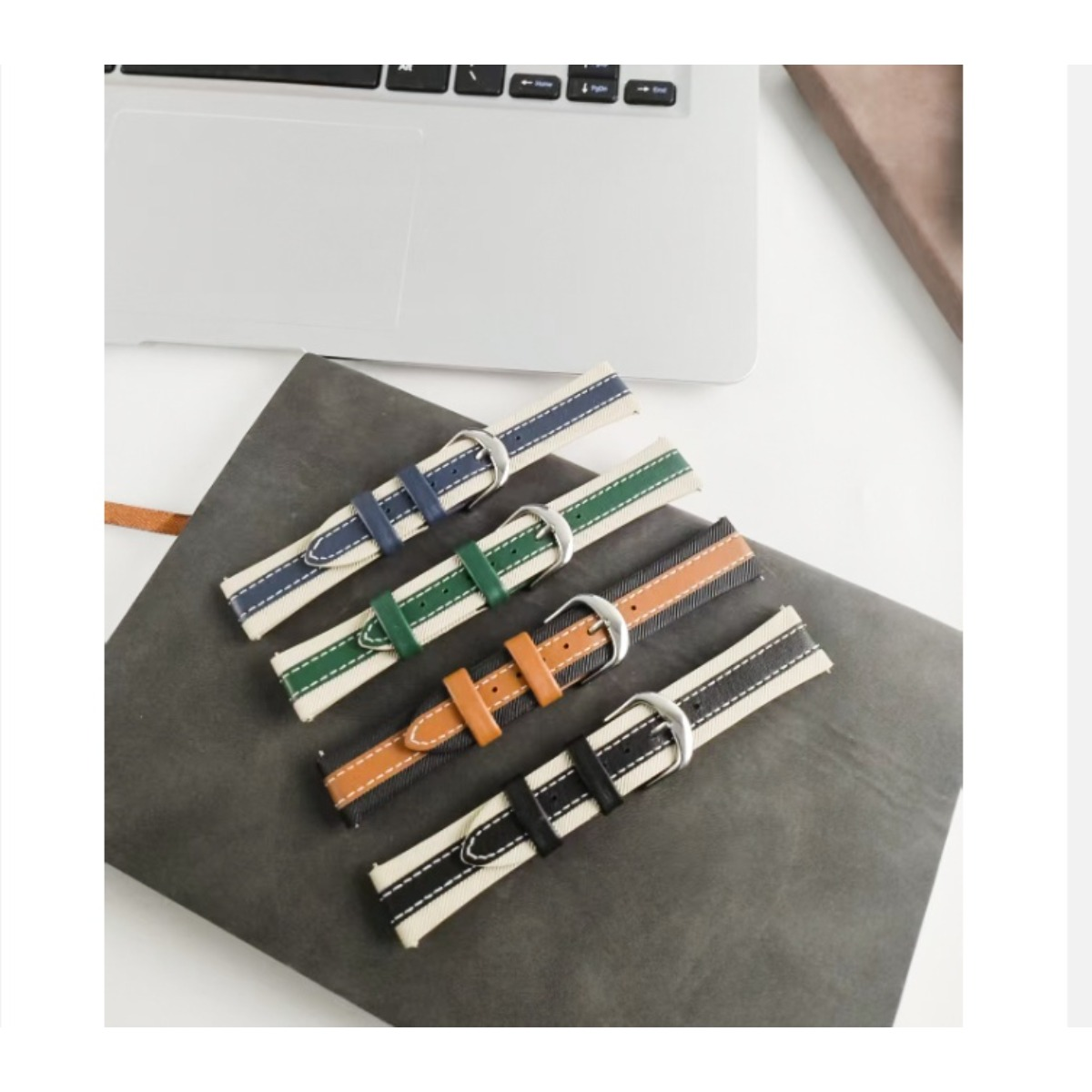 Vier Armbanduhrenarmbänder liegen auf einem dunklen Notizbuch, neben einem Laptop.