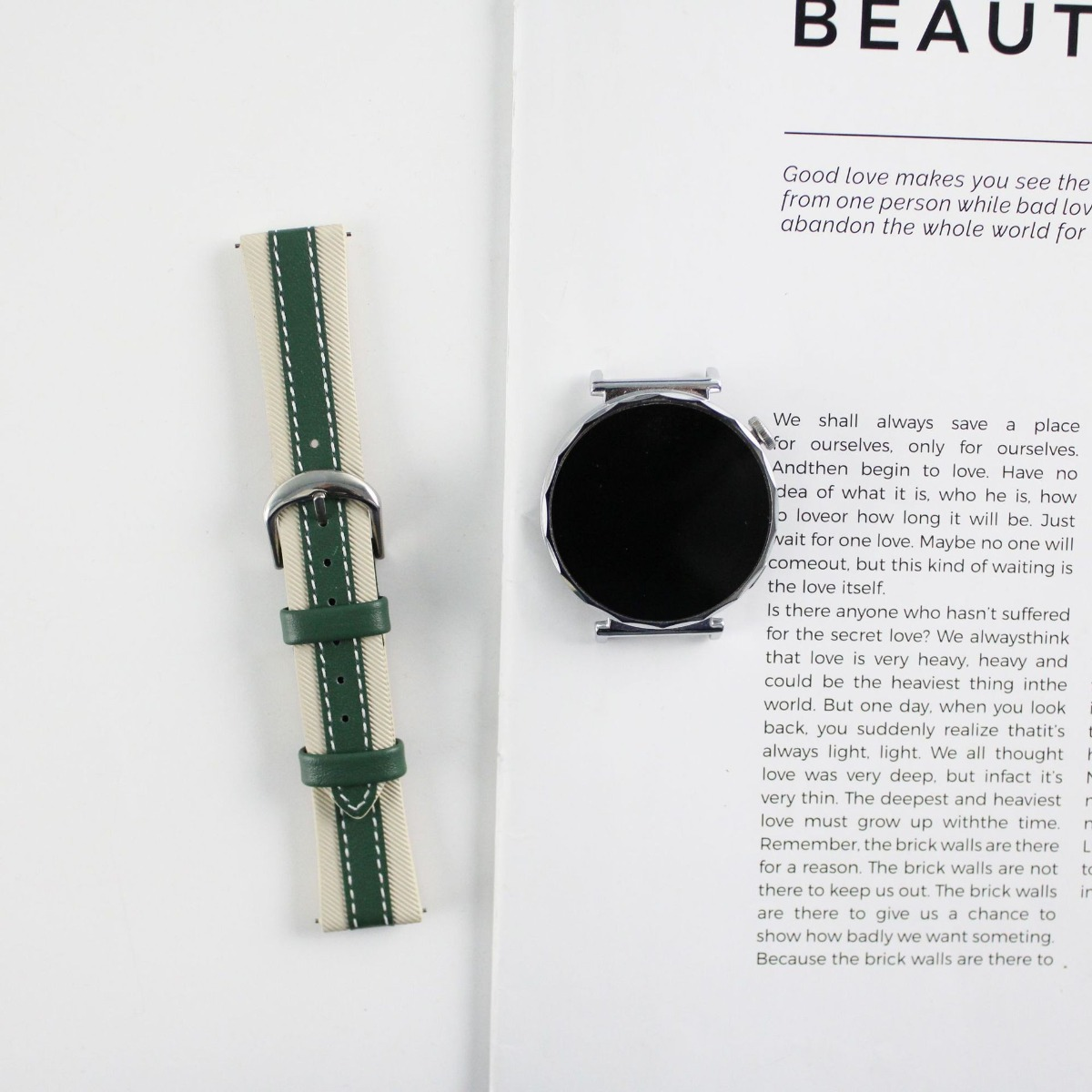 Ein Armband mit Streifen in Beige und Grün und eine Smartwatch mit schwarzem Zifferblatt liegen nebeneinander.