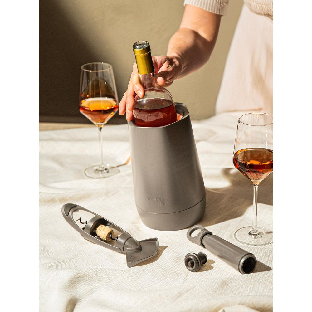Una mano mette una bottiglia di vino in un refrigeratore per vino grigio vicino a due bicchieri.