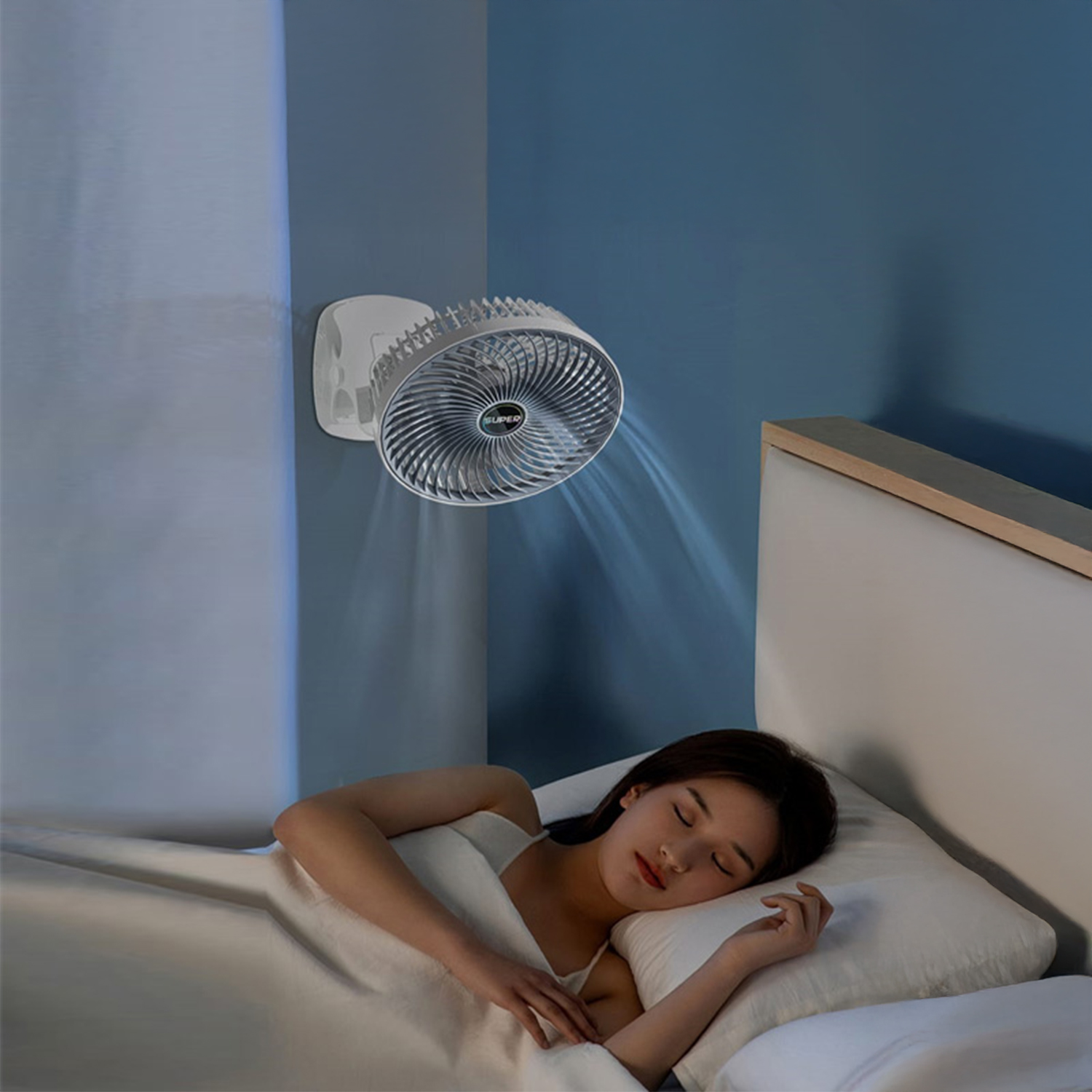 Una donna dorme a letto mentre un ventilatore a parete soffia aria.