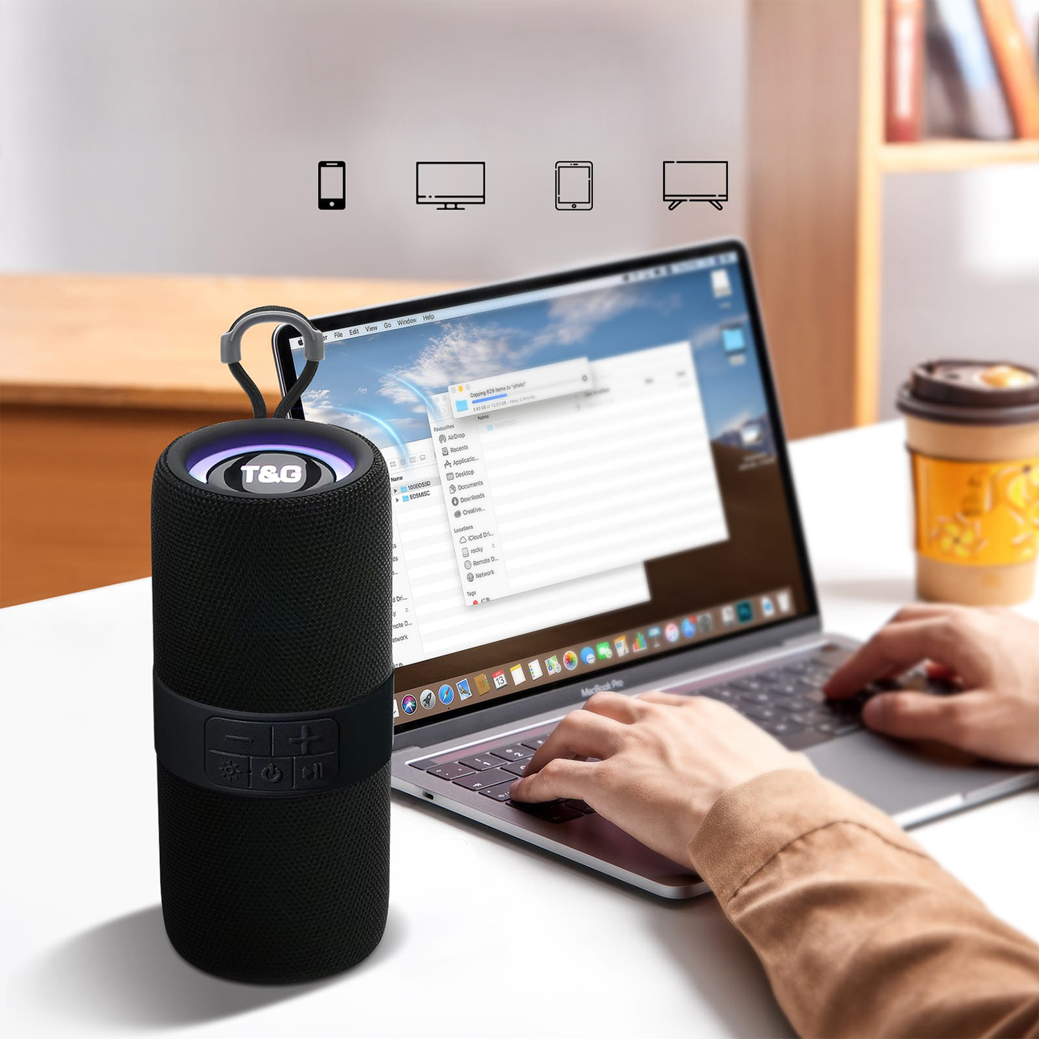 Altoparlante nero accanto a un laptop, una mano digita. Tazza di caffè sullo sfondo.