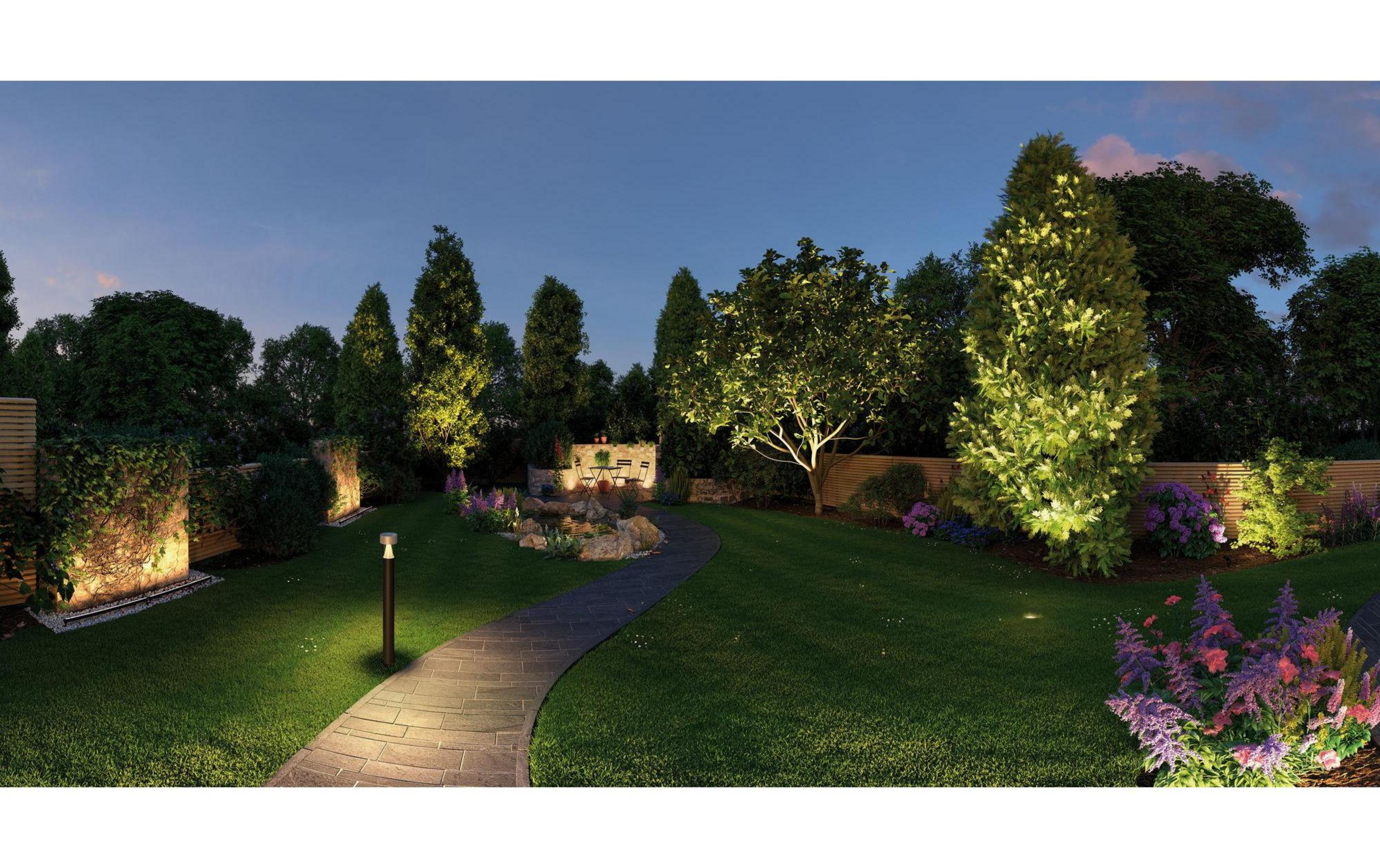 Sentier illuminé menant à un étang avec coin salon. Arbres et fleurs sont éclairés.