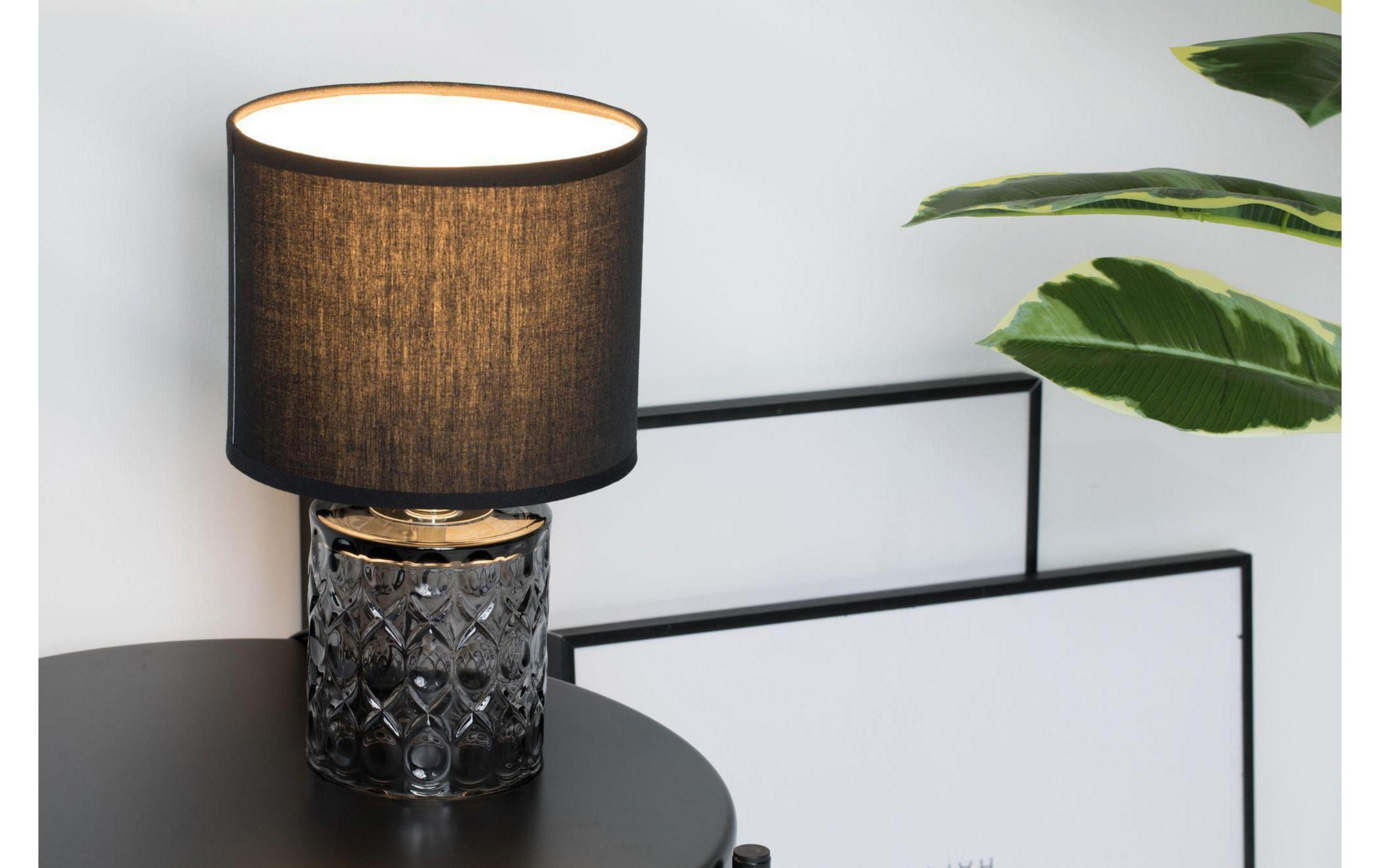 Czarna lampa stołowa ze szklaną podstawą na okrągłym stole.