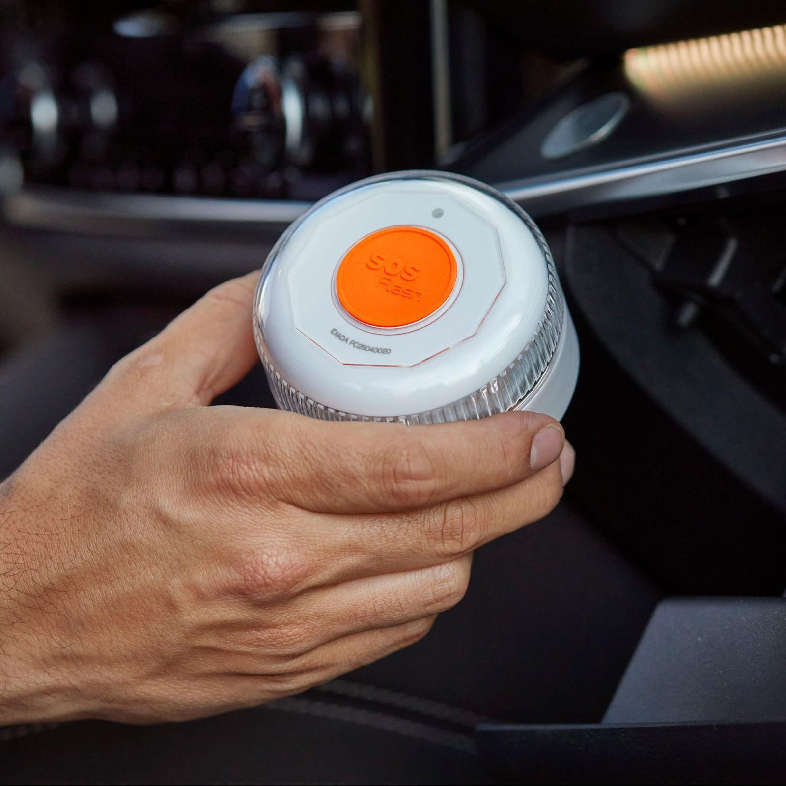 Una mano sostiene una luz estroboscópica SOS blanca con un botón naranja.