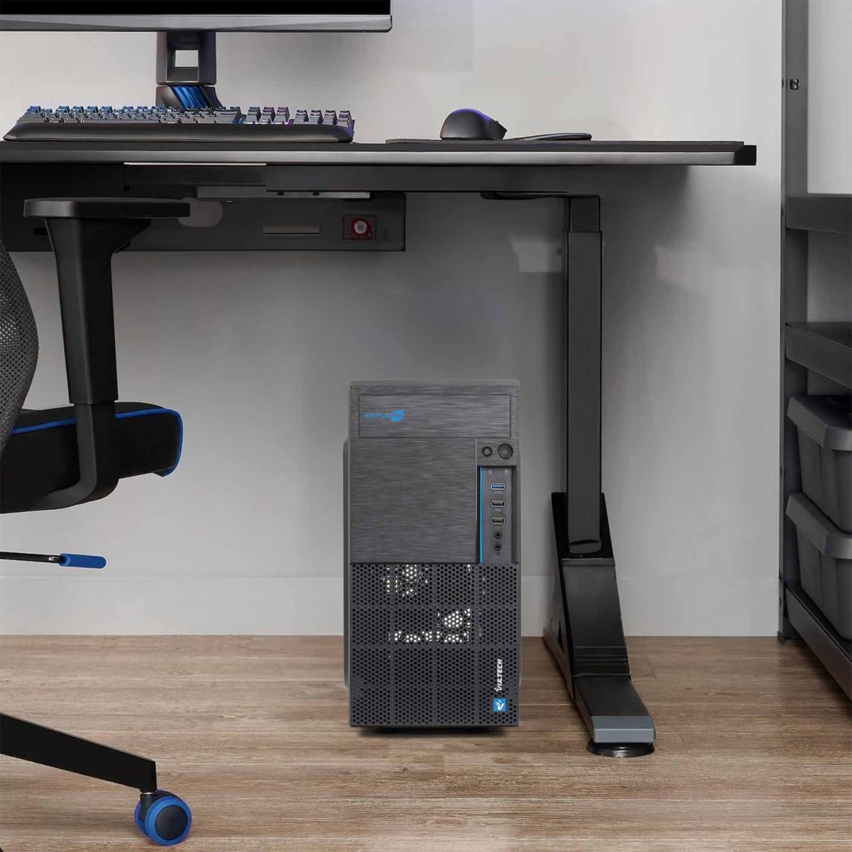 Una torre del computer nera si trova su un pavimento di legno sotto una scrivania.