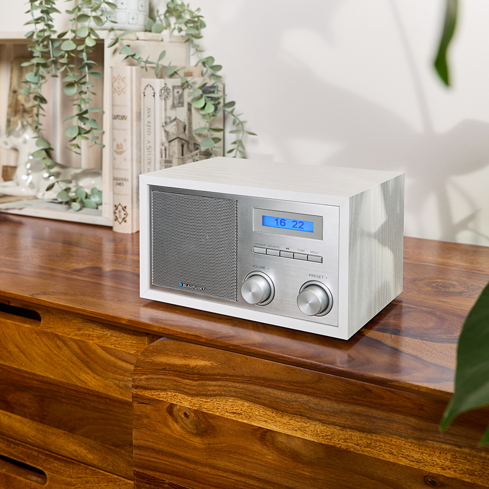 Ein weißes Holzradio mit silberner Front und blauem Display steht auf einer Holzkommode.
