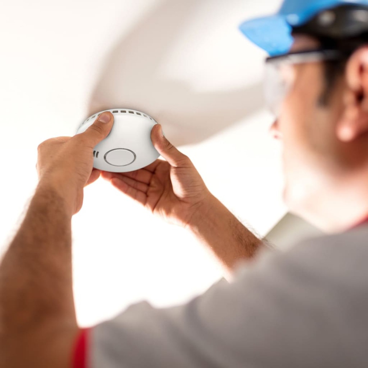 Mężczyzna w kasku instaluje biały czujnik dymu na suficie.