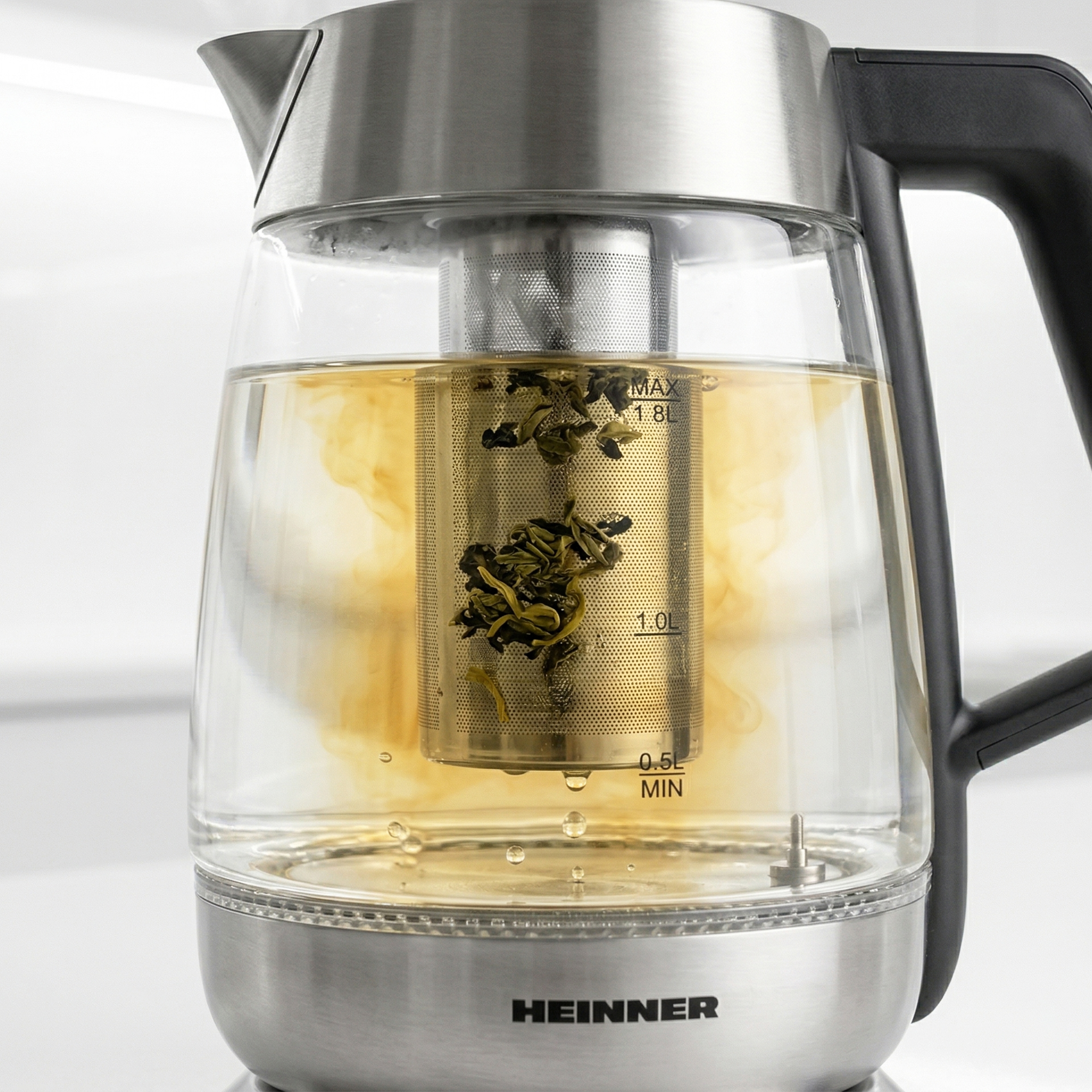 Théière en verre avec infuseur inox et feuilles de thé, eau en infusion.