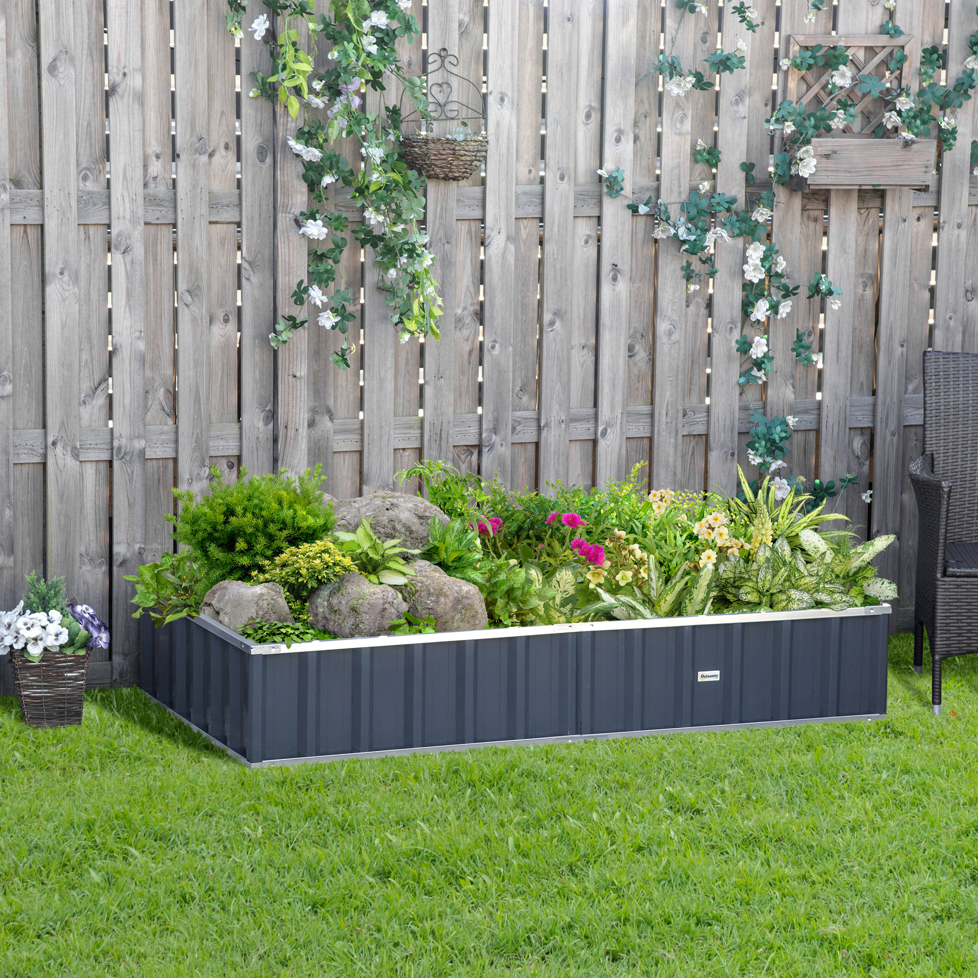 Un bancal elevado gris con plantas y rocas frente a una valla de madera.