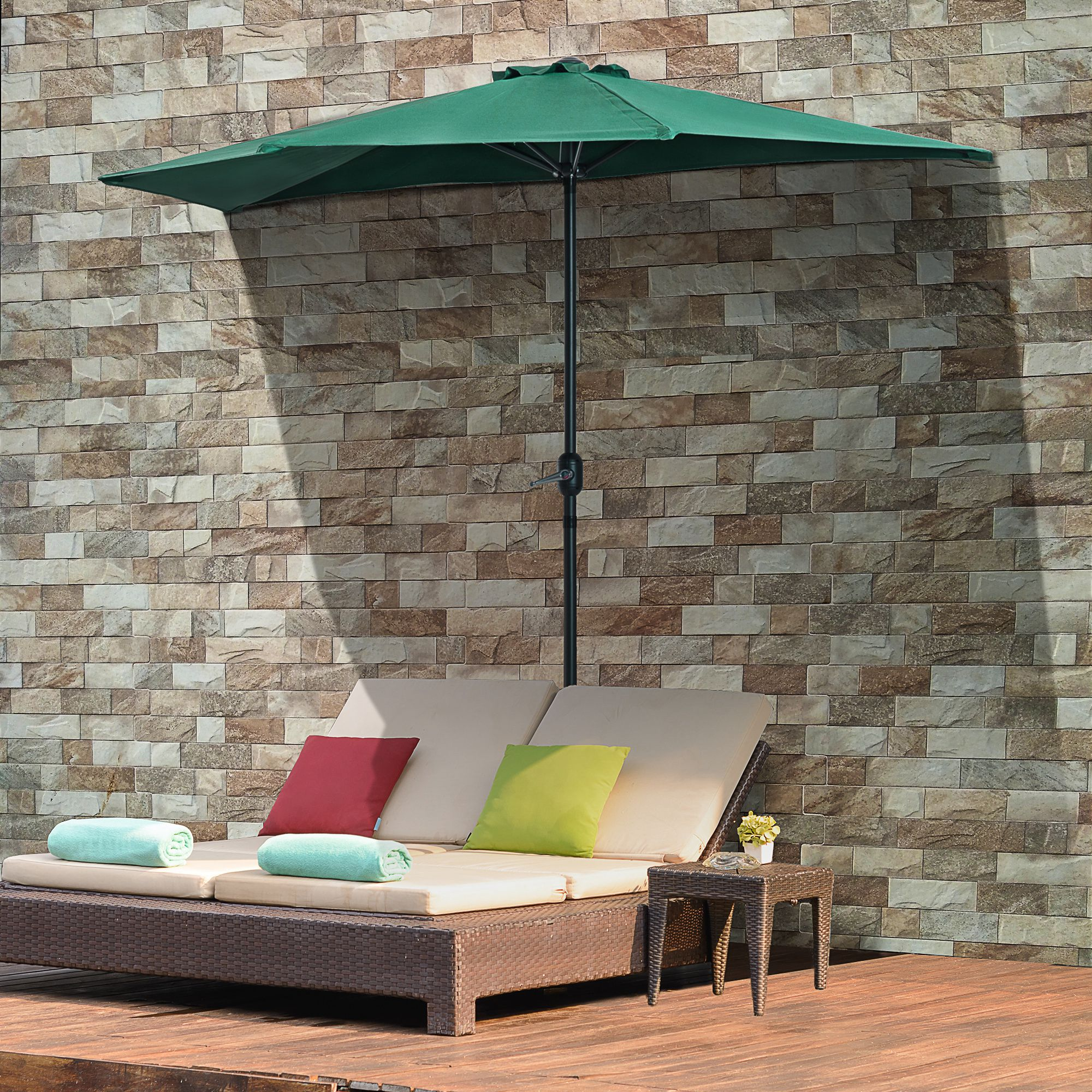 Un lettino prendisole in rattan marrone con cuscini beige, cuscini verdi e rossi, asciugamani e ombrellone.