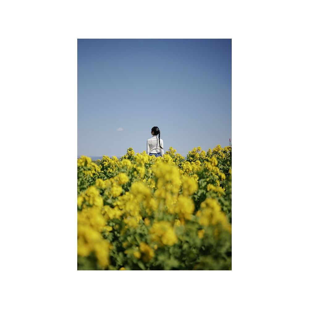 Ein Mädchen mit Zopf steht in einem Feld voller gelber Blumen unter blauem Himmel.