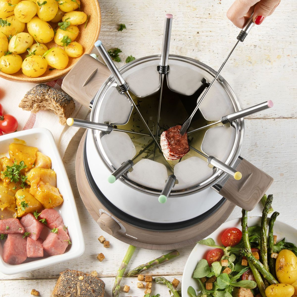 Fondue mit Fleisch, Kartoffeln, Spargel und Salat. Ein Stück Fleisch wird gegart.