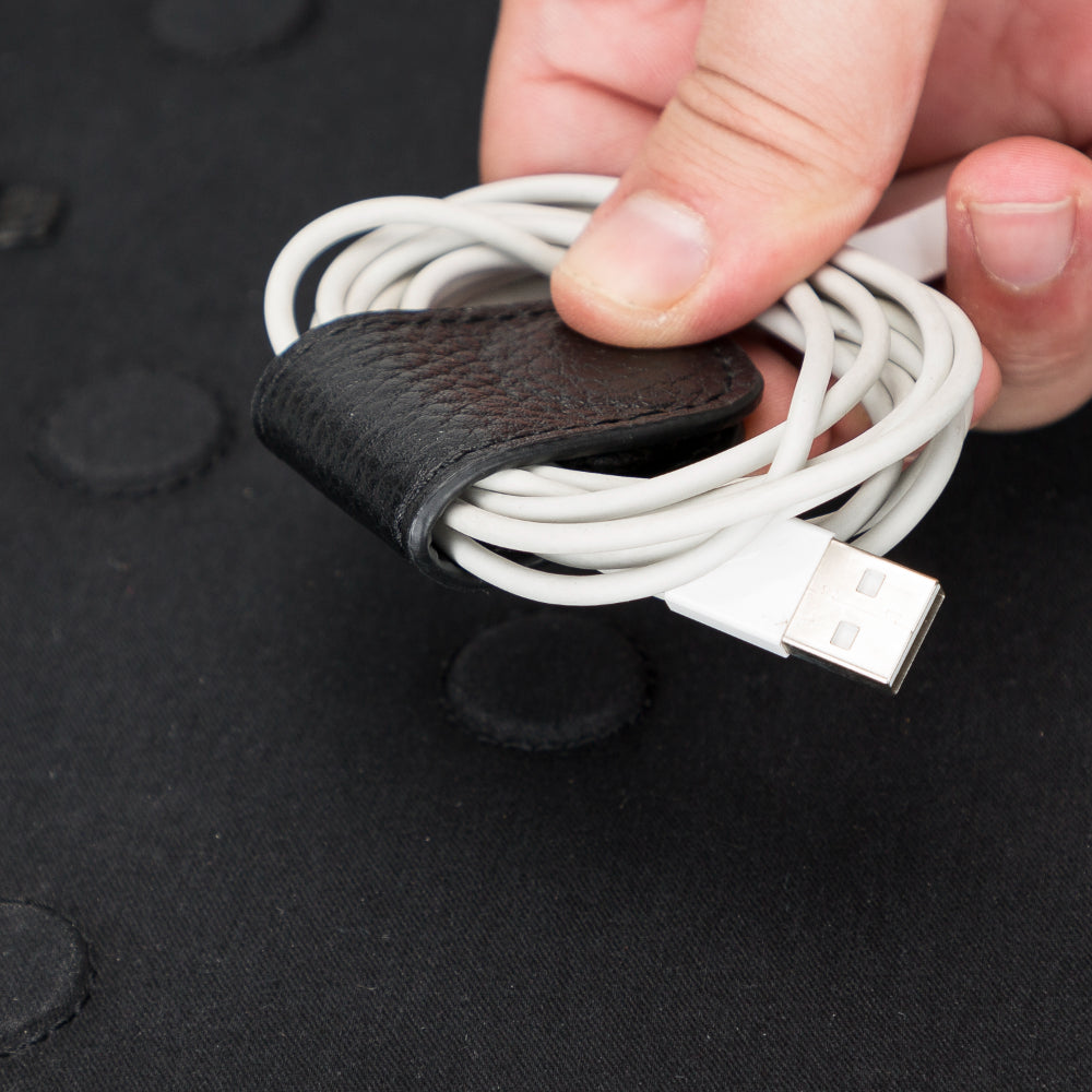 Bir el, siyah deri kablo düzenleyiciye sarılmış beyaz bir USB kablosu tutuyor.