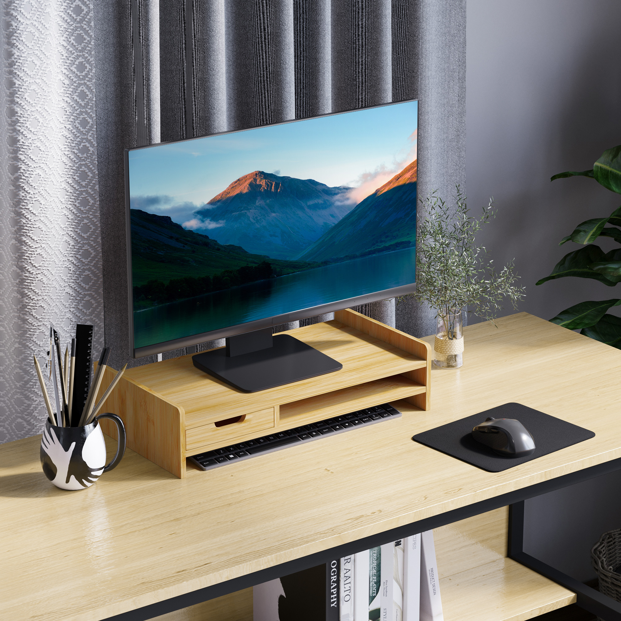 Una scrivania in legno con monitor che mostra montagne, tastiera, mouse e cancelleria.