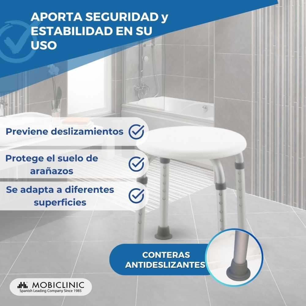 Un taburete blanco en un baño con azulejos grises y bañera. Se ven pies antideslizantes.