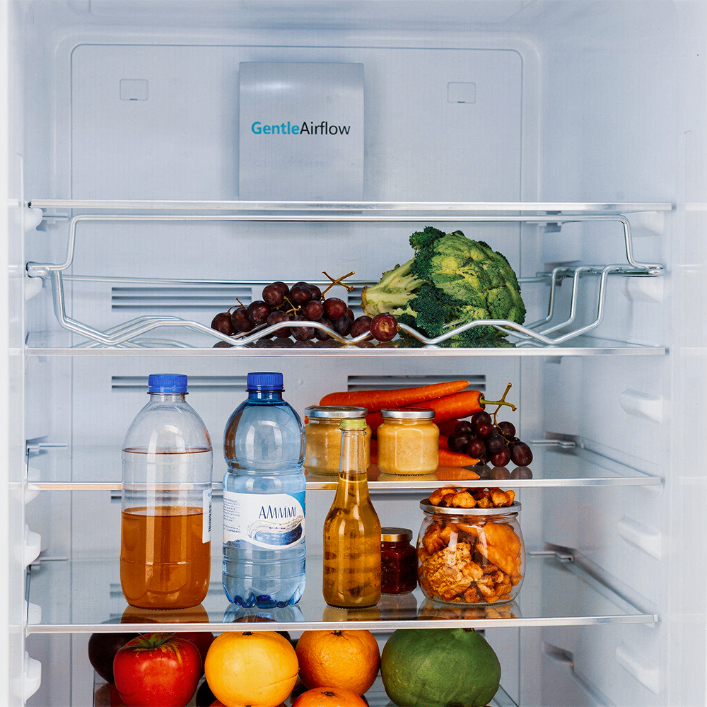 An open refrigerator with fruit, vegetables, bottles, and jars on shelves.