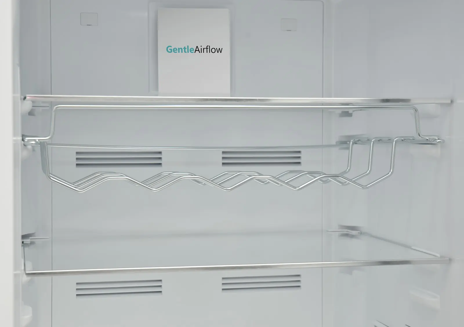 Inside view of an empty refrigerator with a bottle rack and air vents.