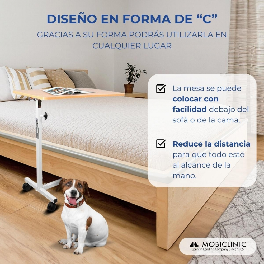 Una mesa auxiliar ajustable con ruedas al lado de una cama. Un perro sentado.