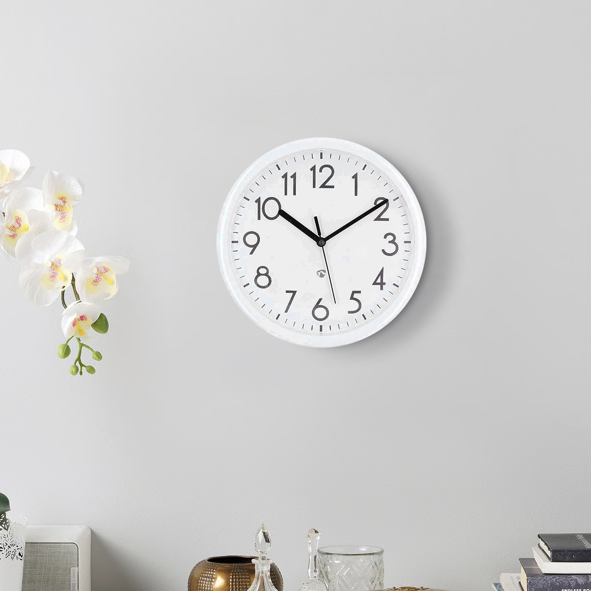 Eine weiße runde Uhr mit schwarzen Ziffern und Zeigern hängt an einer grauen Wand.
