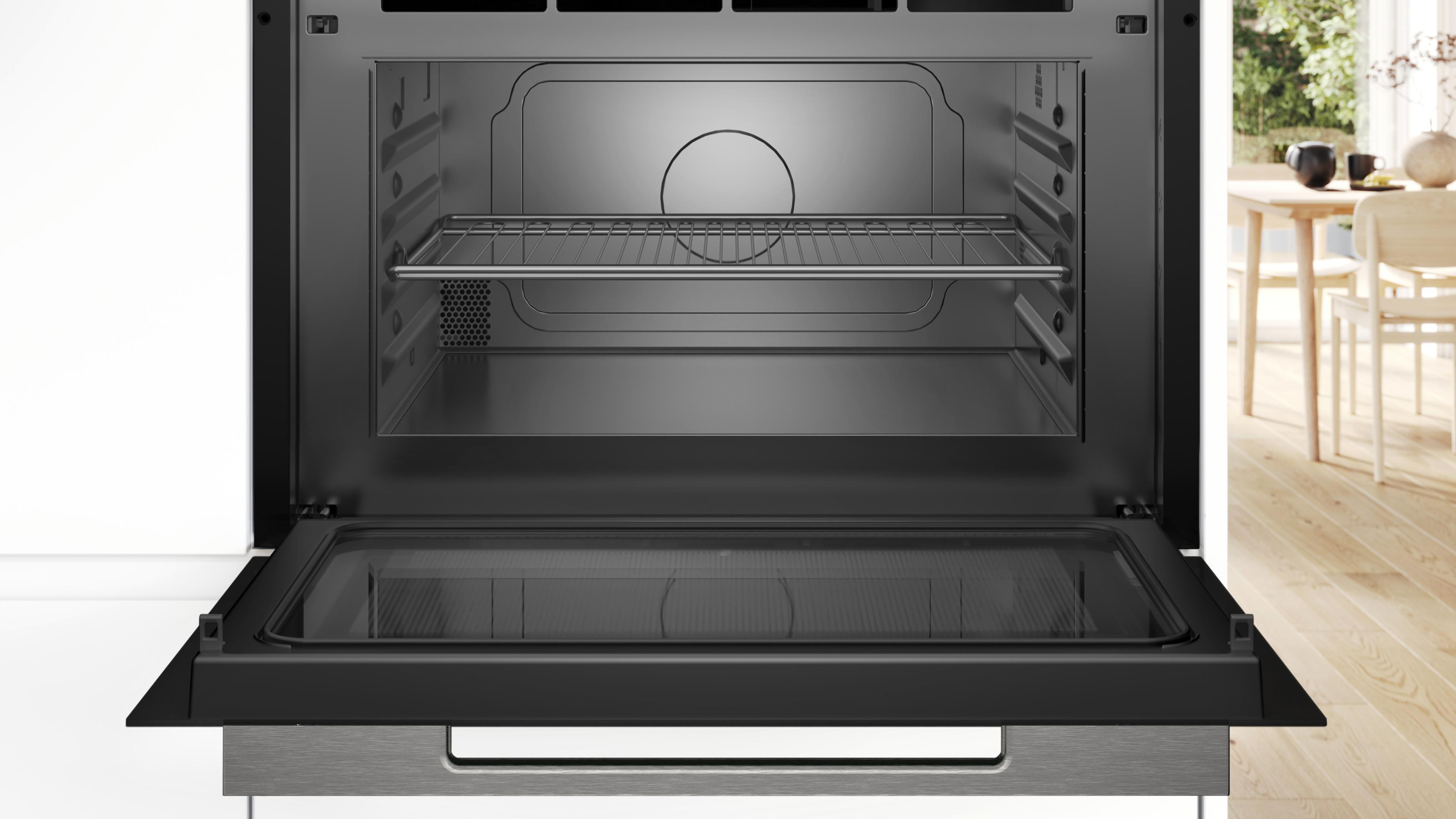 An open built-in oven with a rack and a glass door. Dining area in the background.