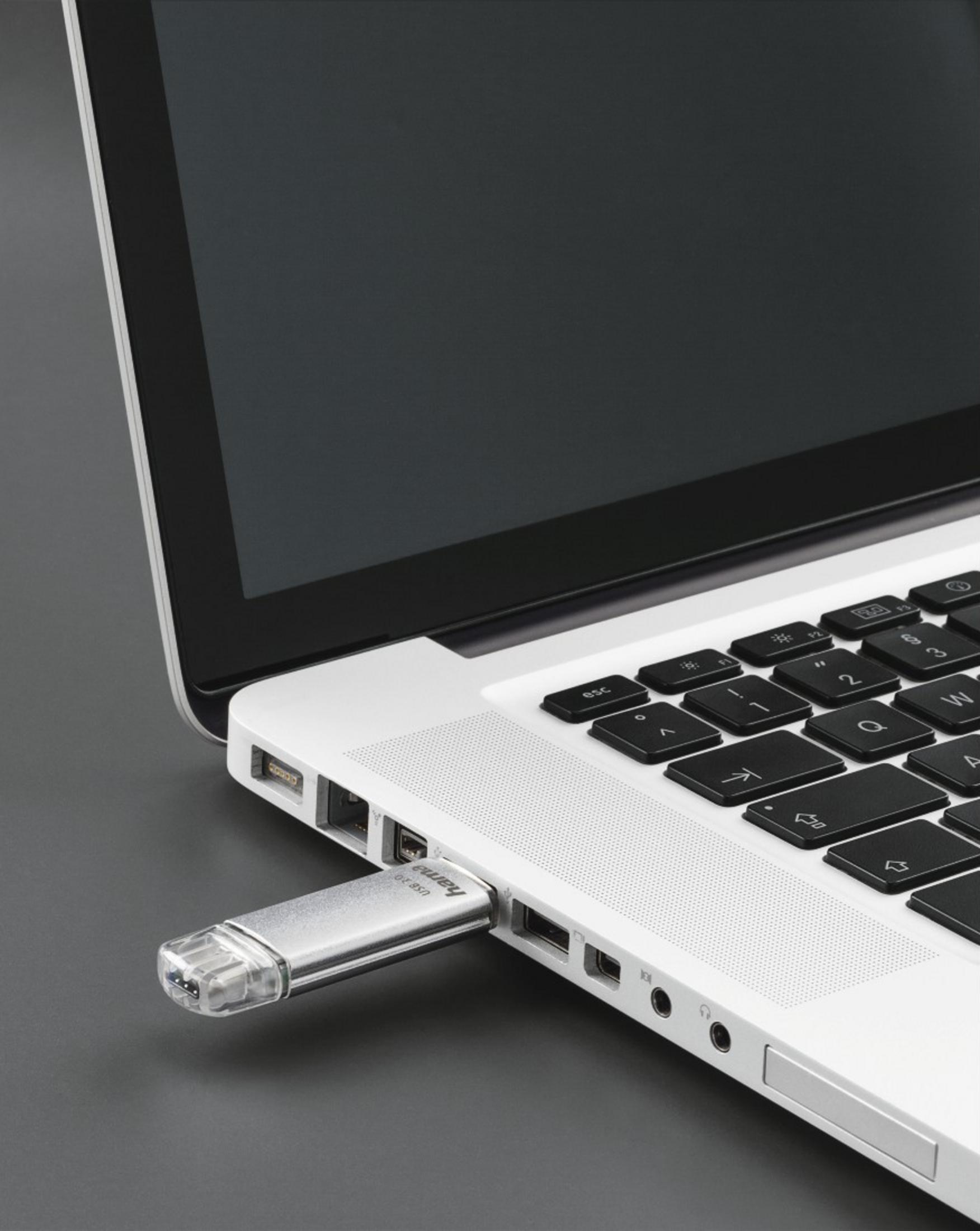 Une clé USB argentée est branchée sur un ordinateur portable. Clavier et écran visibles.