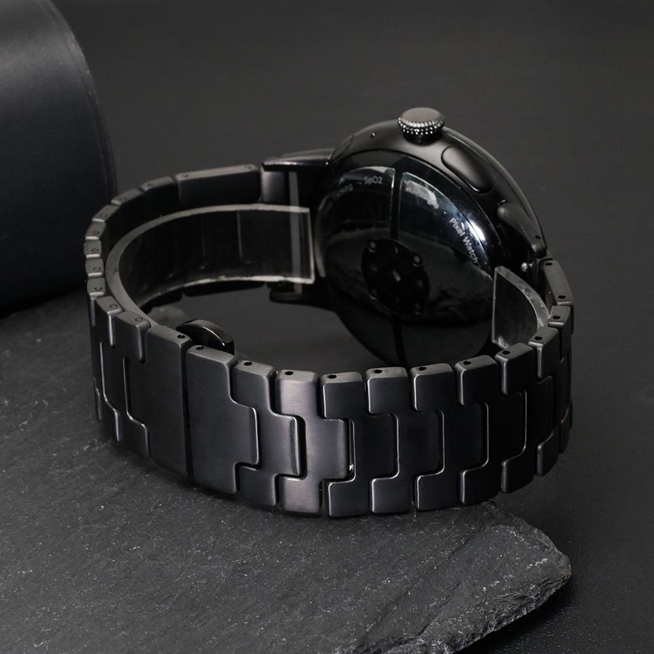 Uno smartwatch nero con cinturino in metallo su una superficie scura.