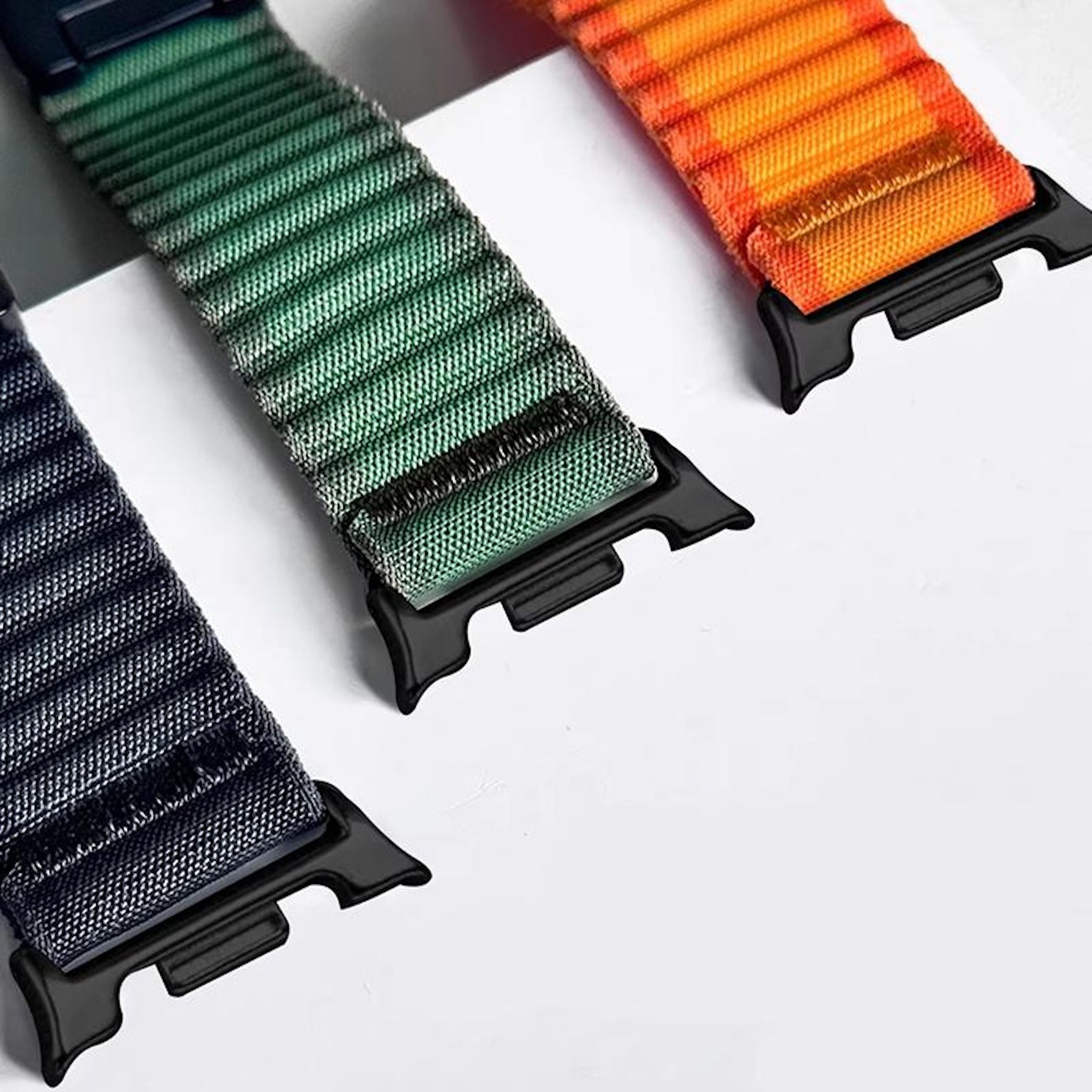 Tre cinturini per orologio blu, verdi e arancioni con connettori neri su sfondo bianco.
