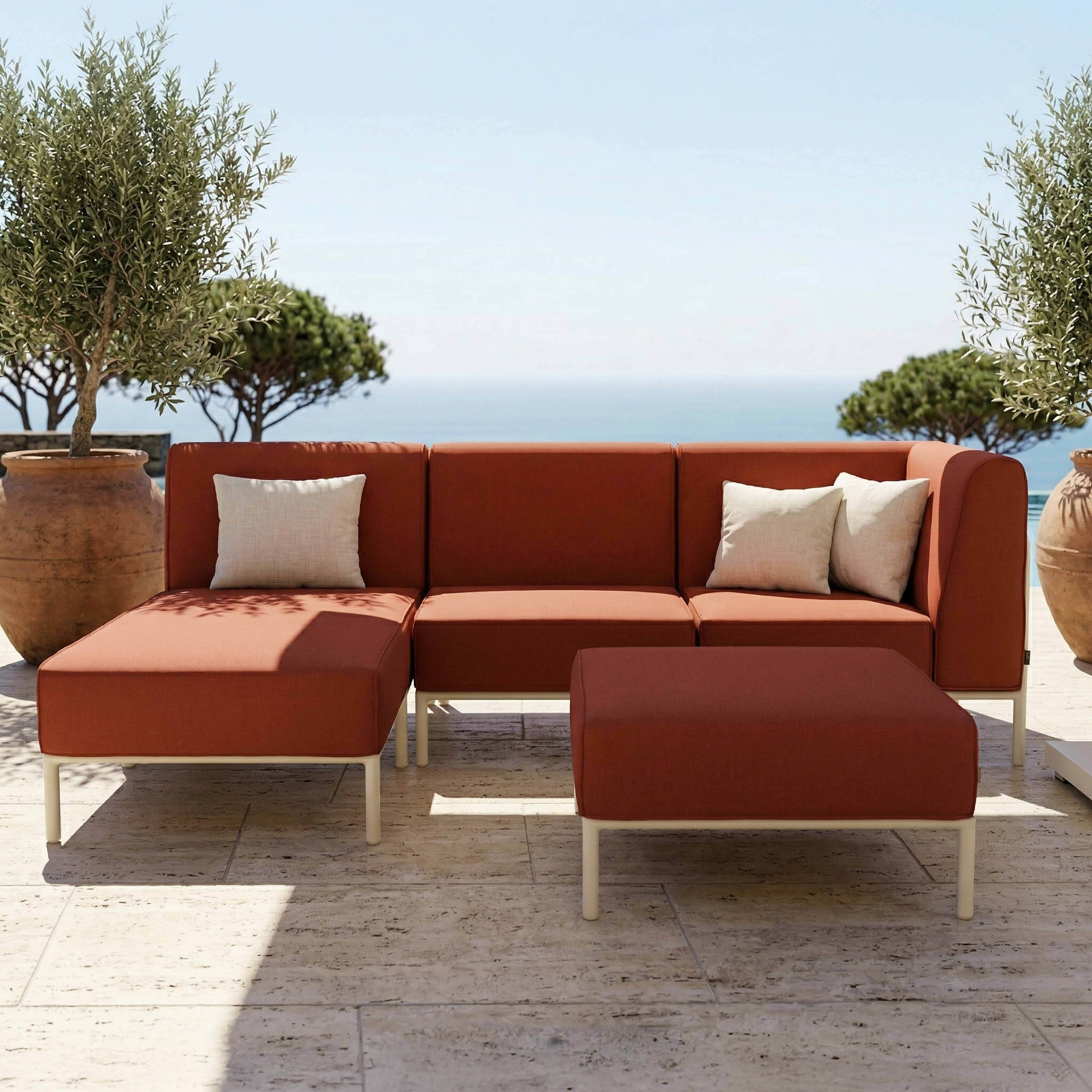 Orange Lounge-Möbel mit weißen Kissen stehen auf einer Steinterrasse am Meer.