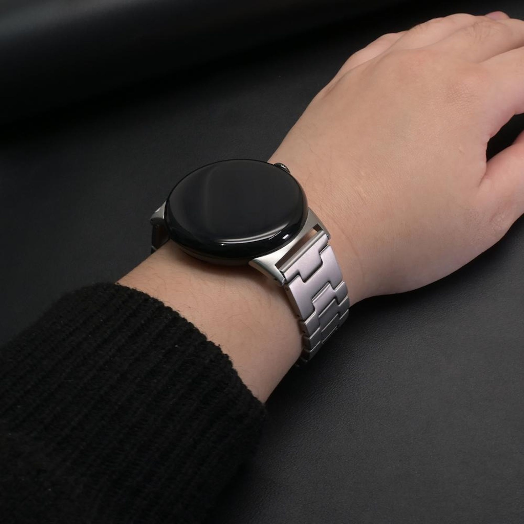 Eine Person trägt eine silberne Smartwatch mit einem Gliederarmband am linken Handgelenk.