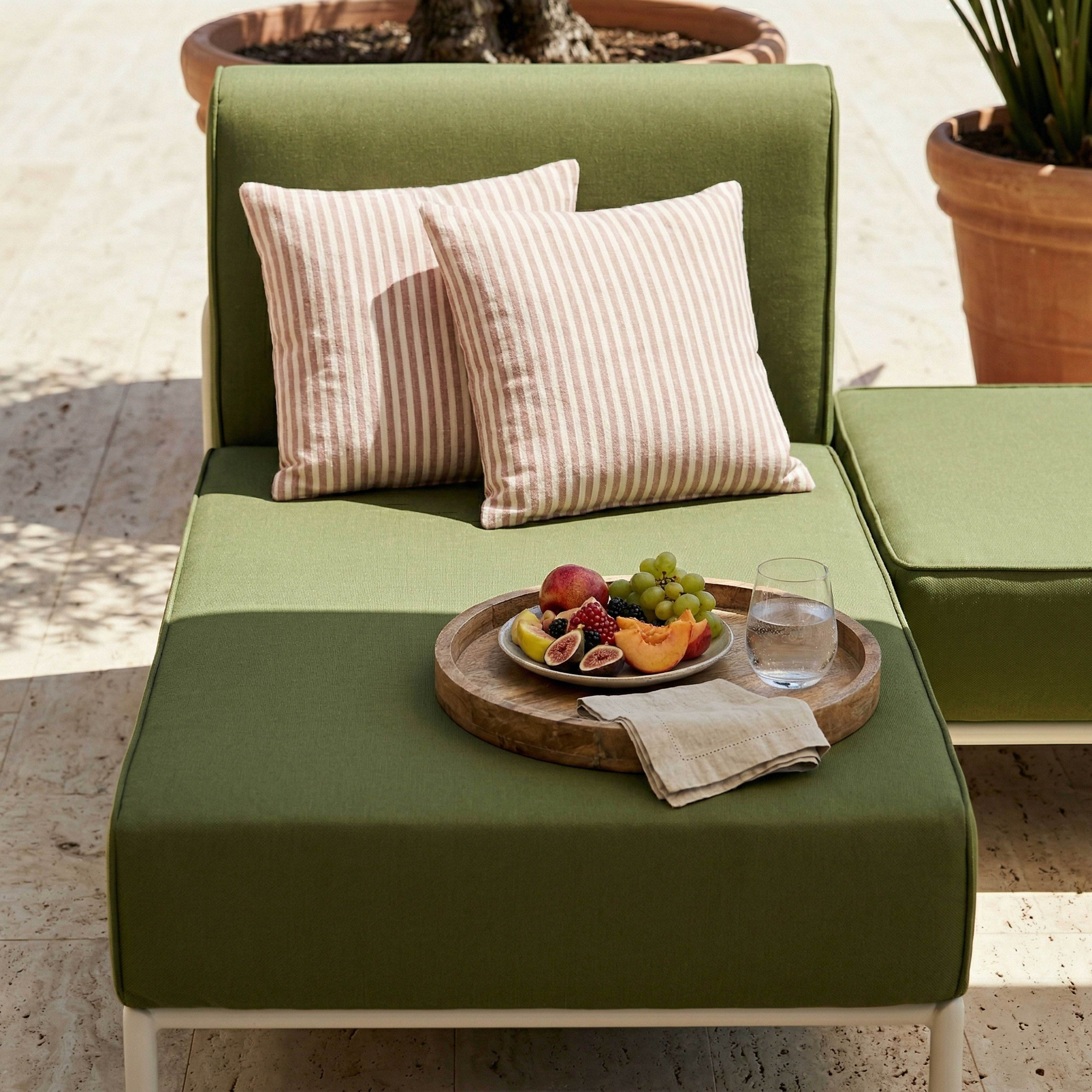 Grünes Outdoor-Sofa mit gestreiften Kissen, Obstschale und Wasserglas.